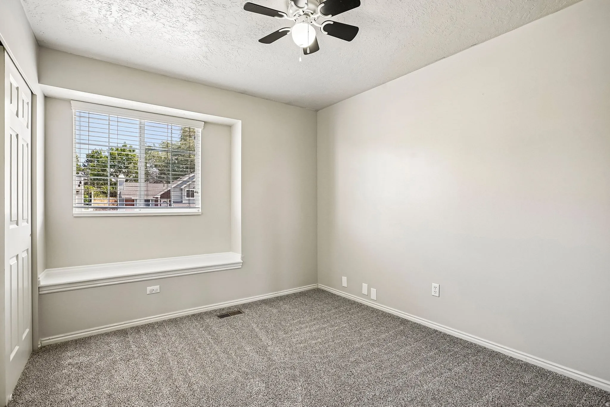 Room featuring light gray carpet, a window with horizontal blinds, a built-in window seat, a ceiling fan with light, and a bi-fold closet door