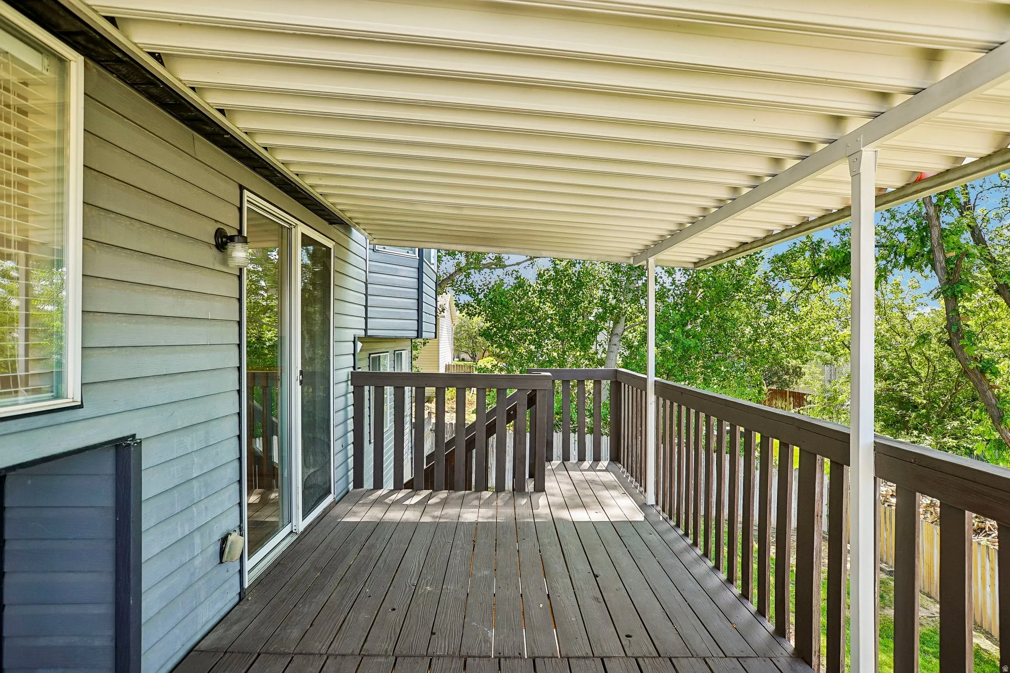 Expansive wood-finish deck with a solid wood railing system, covered by a slatted patio roof
