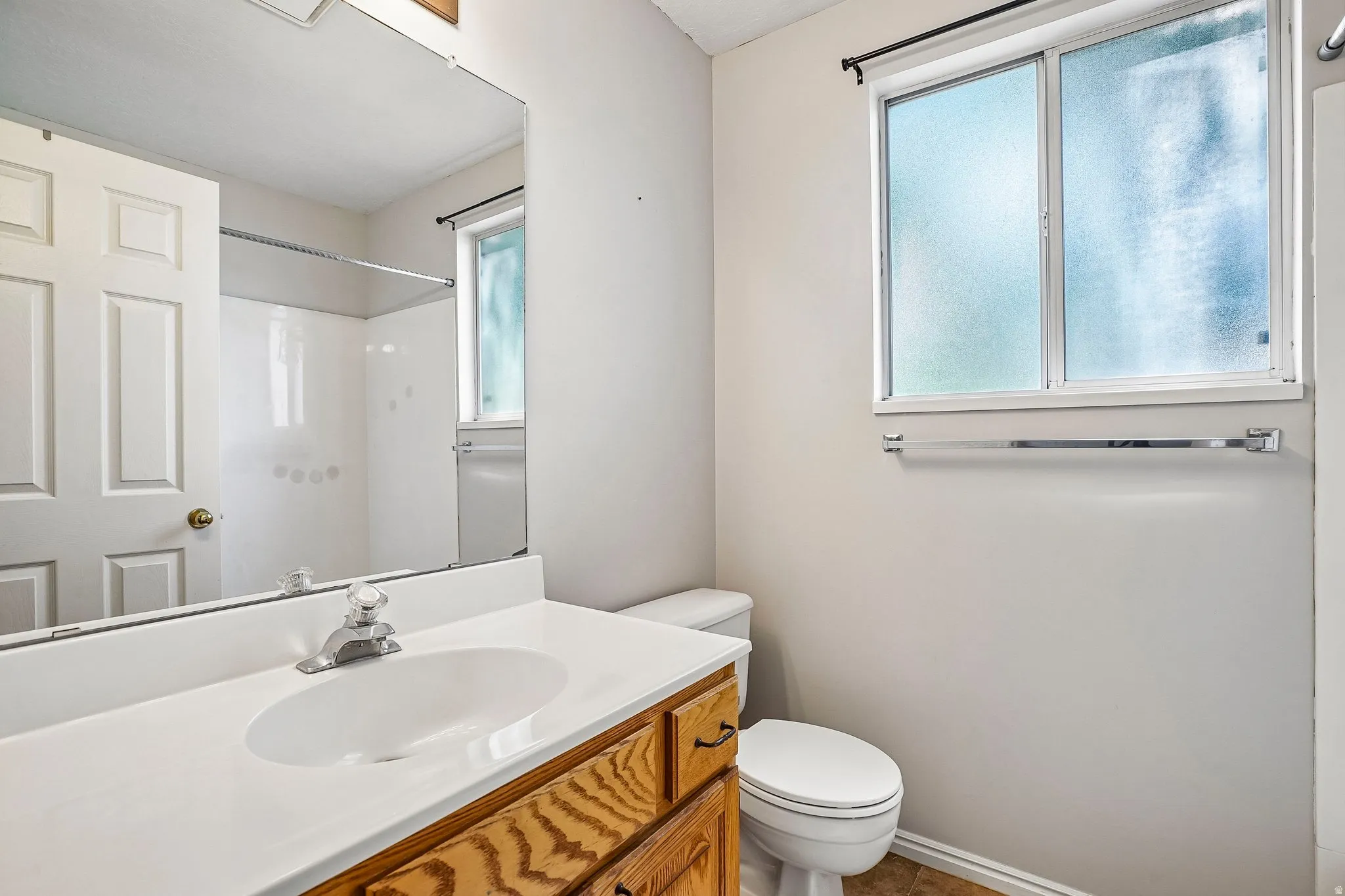 Bathroom featuring a frosted window, wood-finish vanity, integrated sink, and a shower/tub combination with a white surround