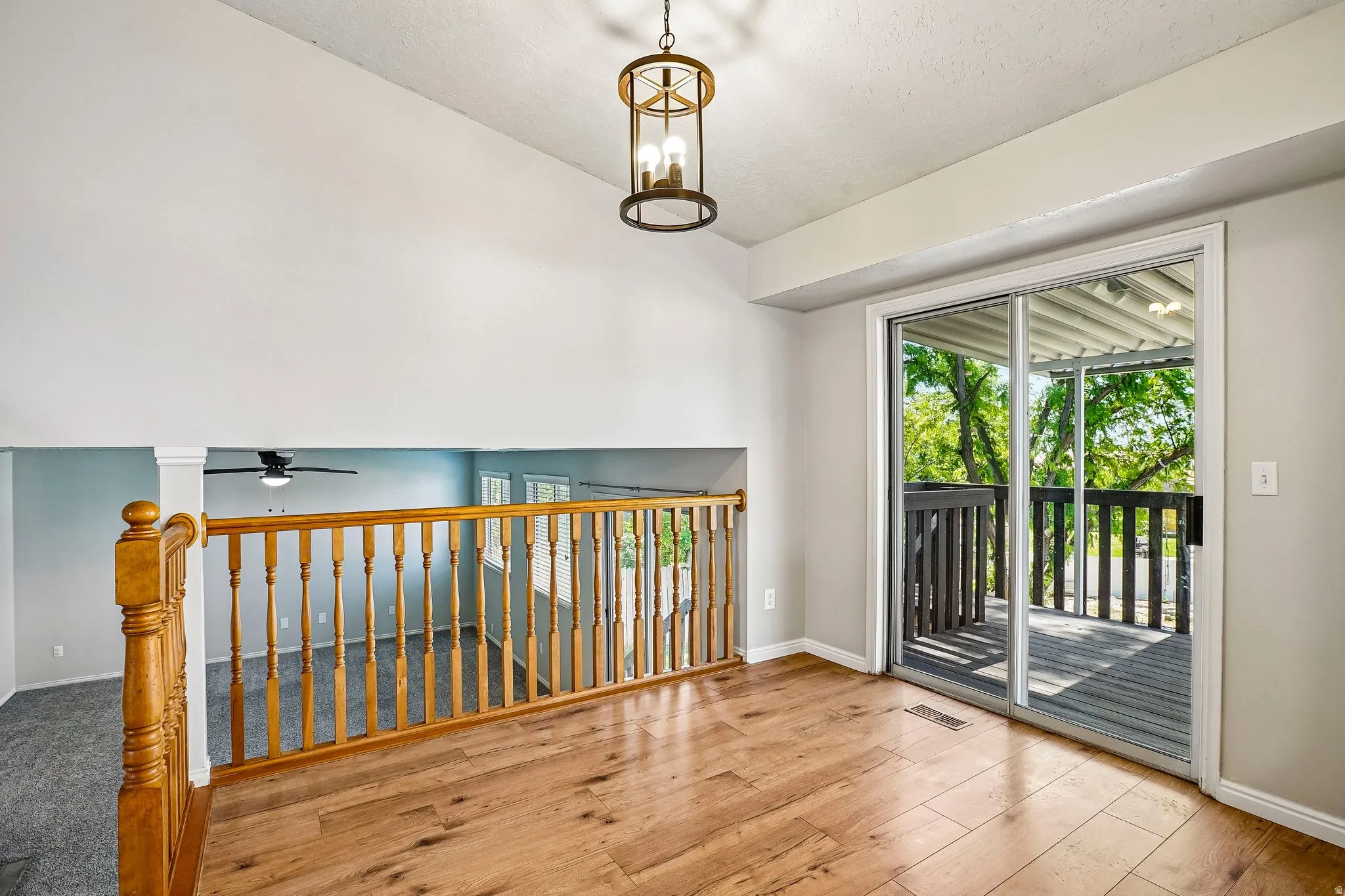 Upper-level landing featuring wood-finish flooring, an open wood railing overlooking a lower space, and a sliding glass door leading to an outdoor deck