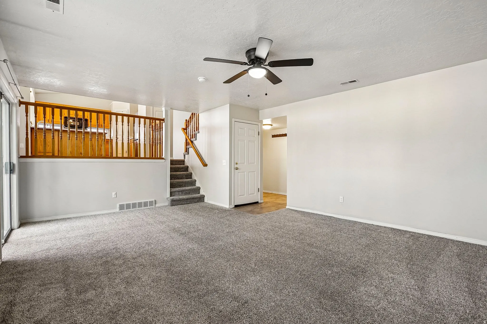 Spacious carpeted living area featuring a ceiling fan, white walls, and a sliding glass door