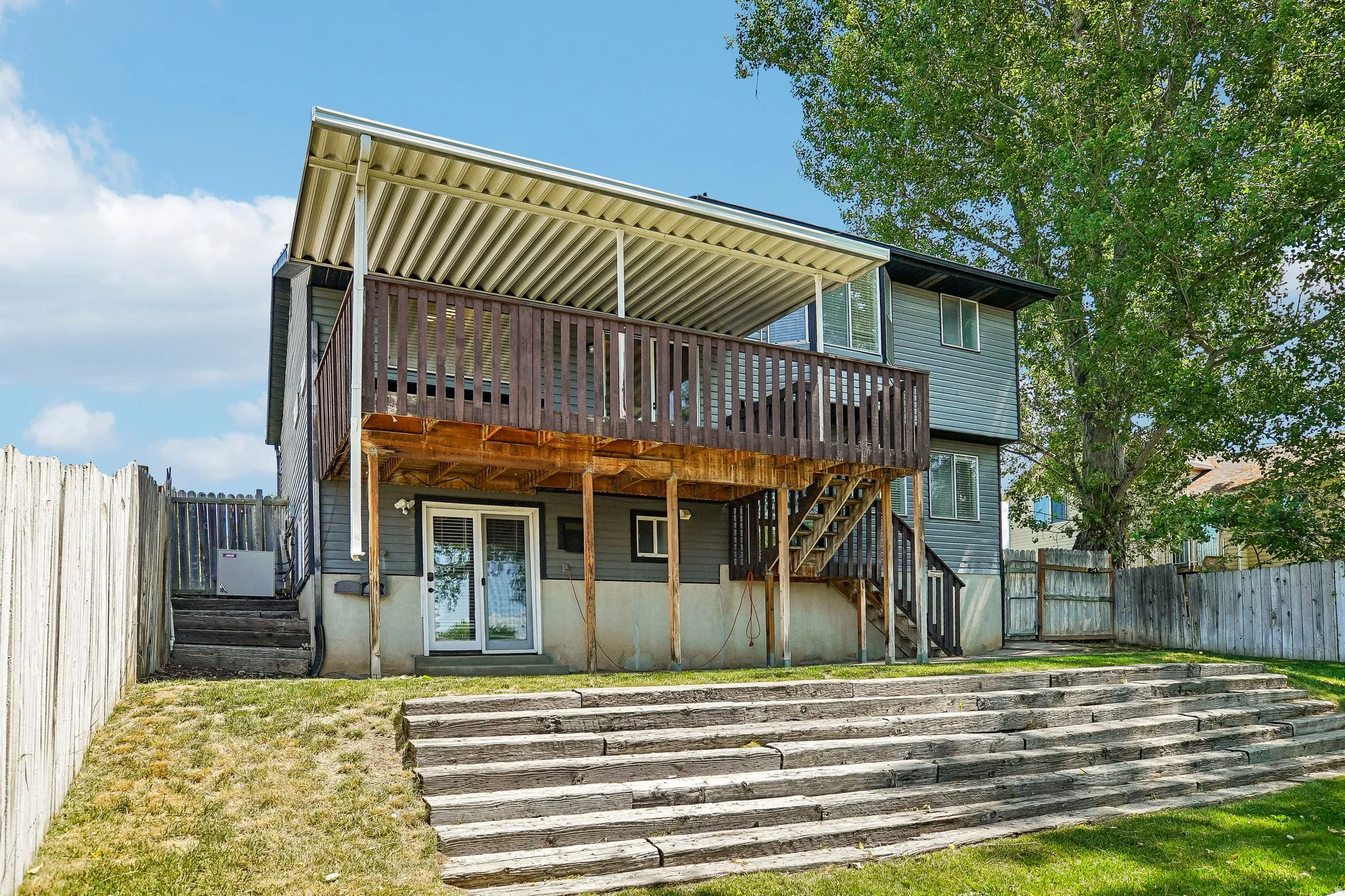 Multi-level backyard featuring a spacious wood deck with slatted railing, a full-coverage patio cover, and sliding glass door access