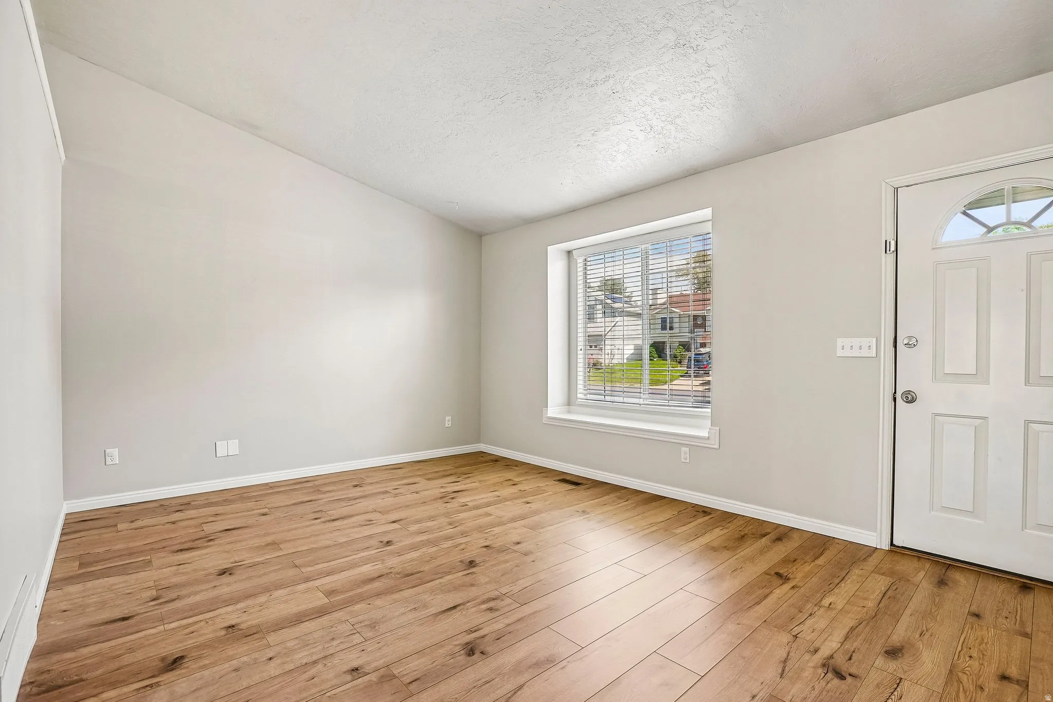 Entry area featuring wood-finish flooring, a white paneled front door with an arched window insert, and a large window with blinds