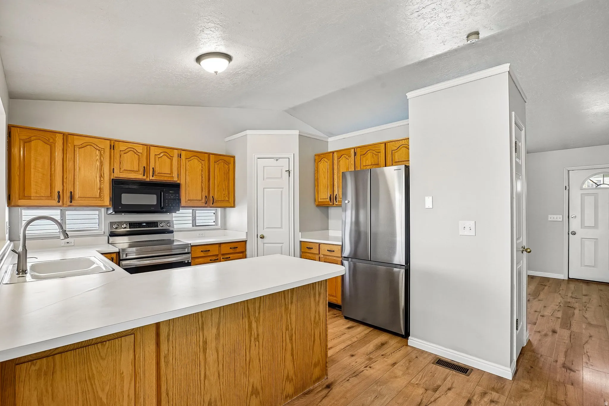 Kitchen featuring wood cabinetry, white countertops, a stainless steel refrigerator, and wood-finish flooring