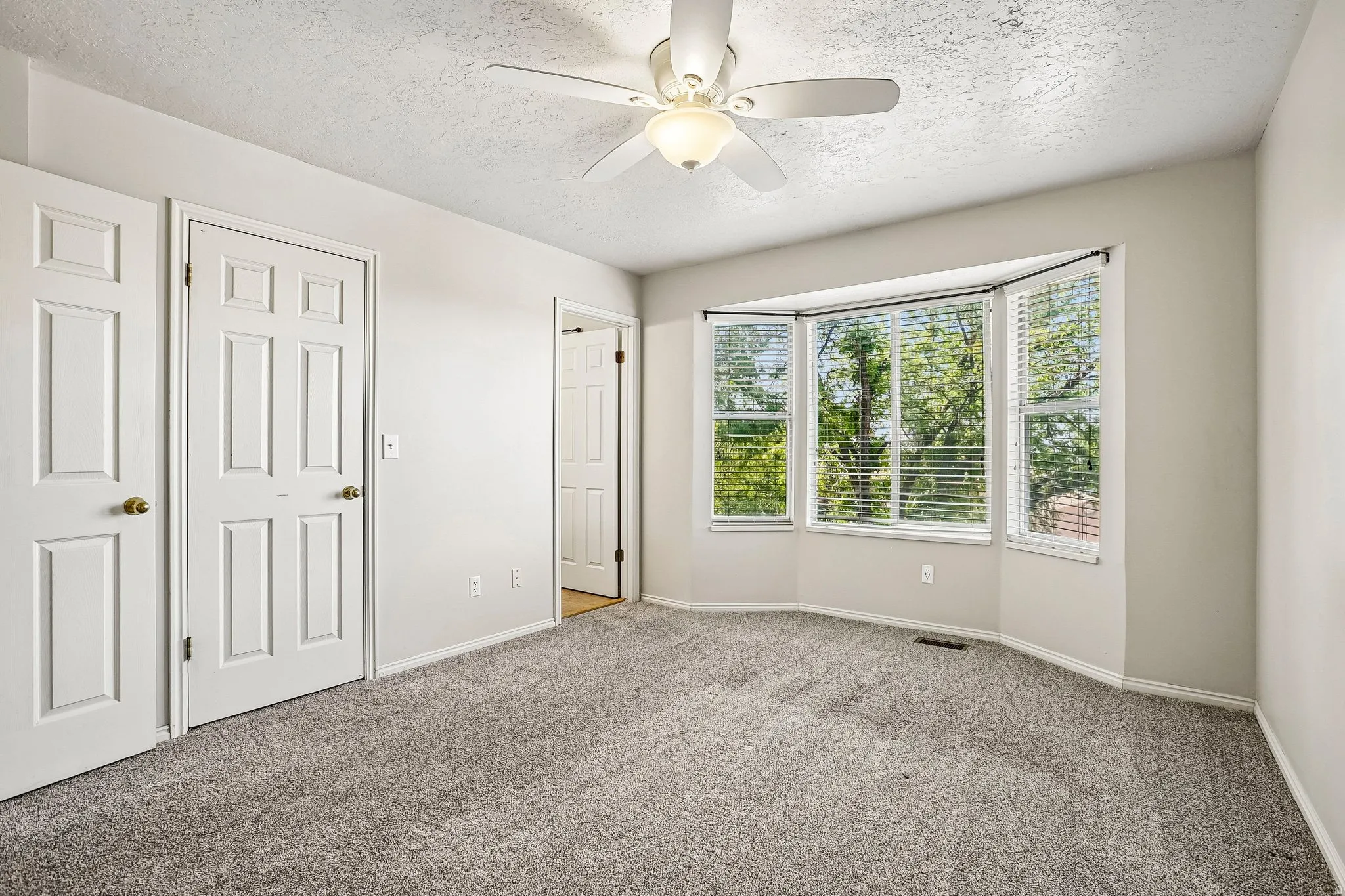 Spacious room featuring a bay window, ceiling fan with integrated lighting, two panel doors, and neutral carpeting