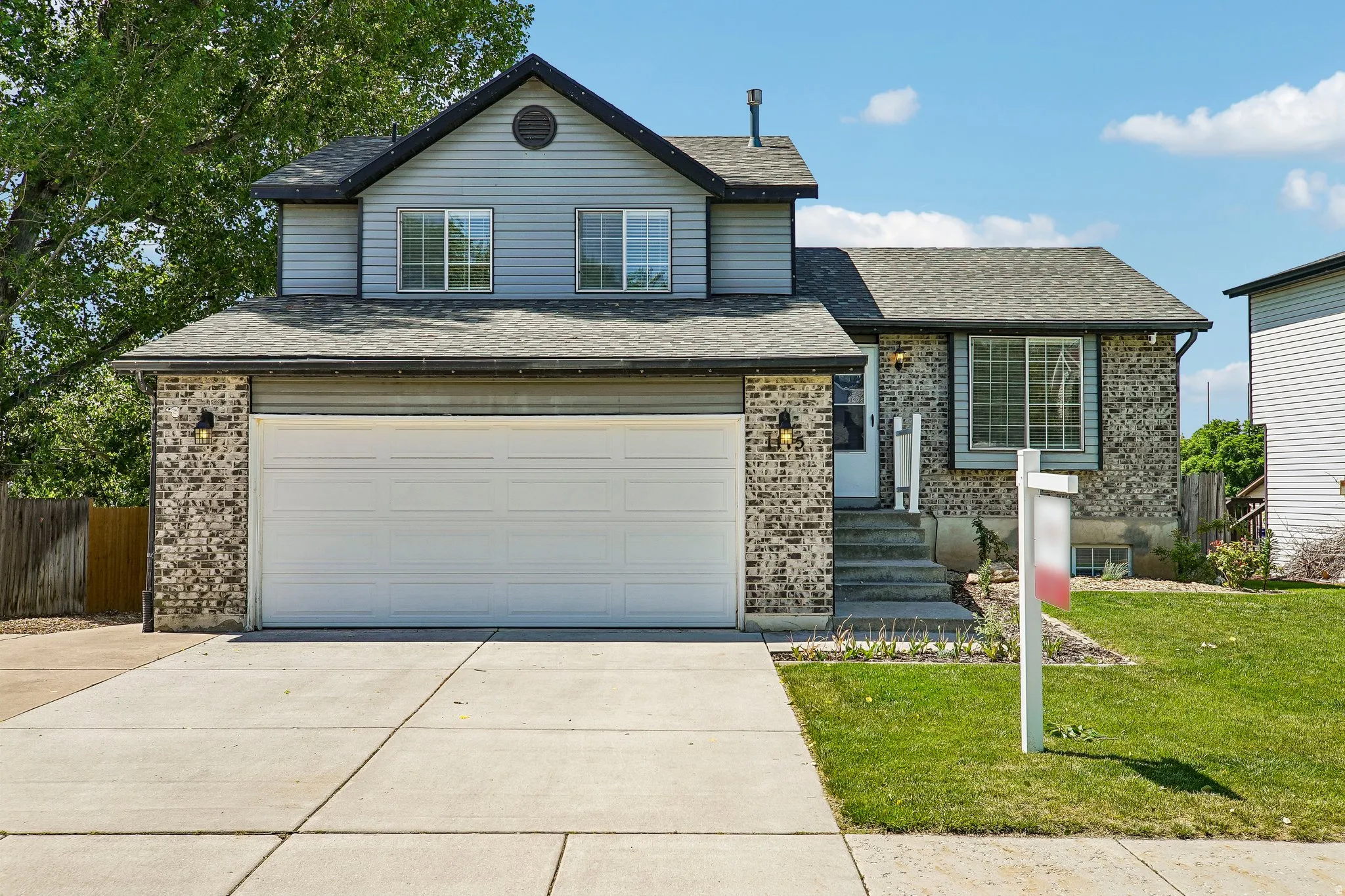Exterior facade with brick and siding accents, featuring a two-car garage, concrete driveway, and front entryway with steps