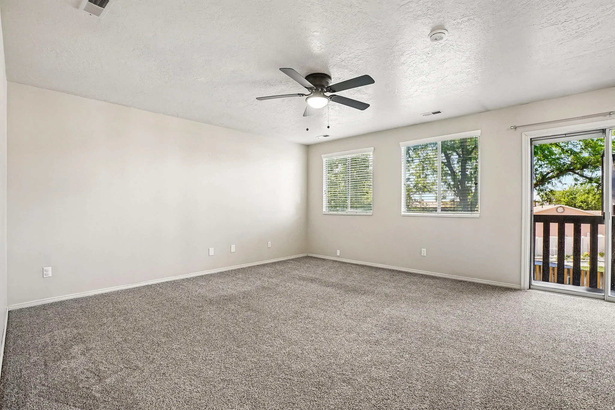 Spacious room featuring neutral walls, gray carpet, and a ceiling fan