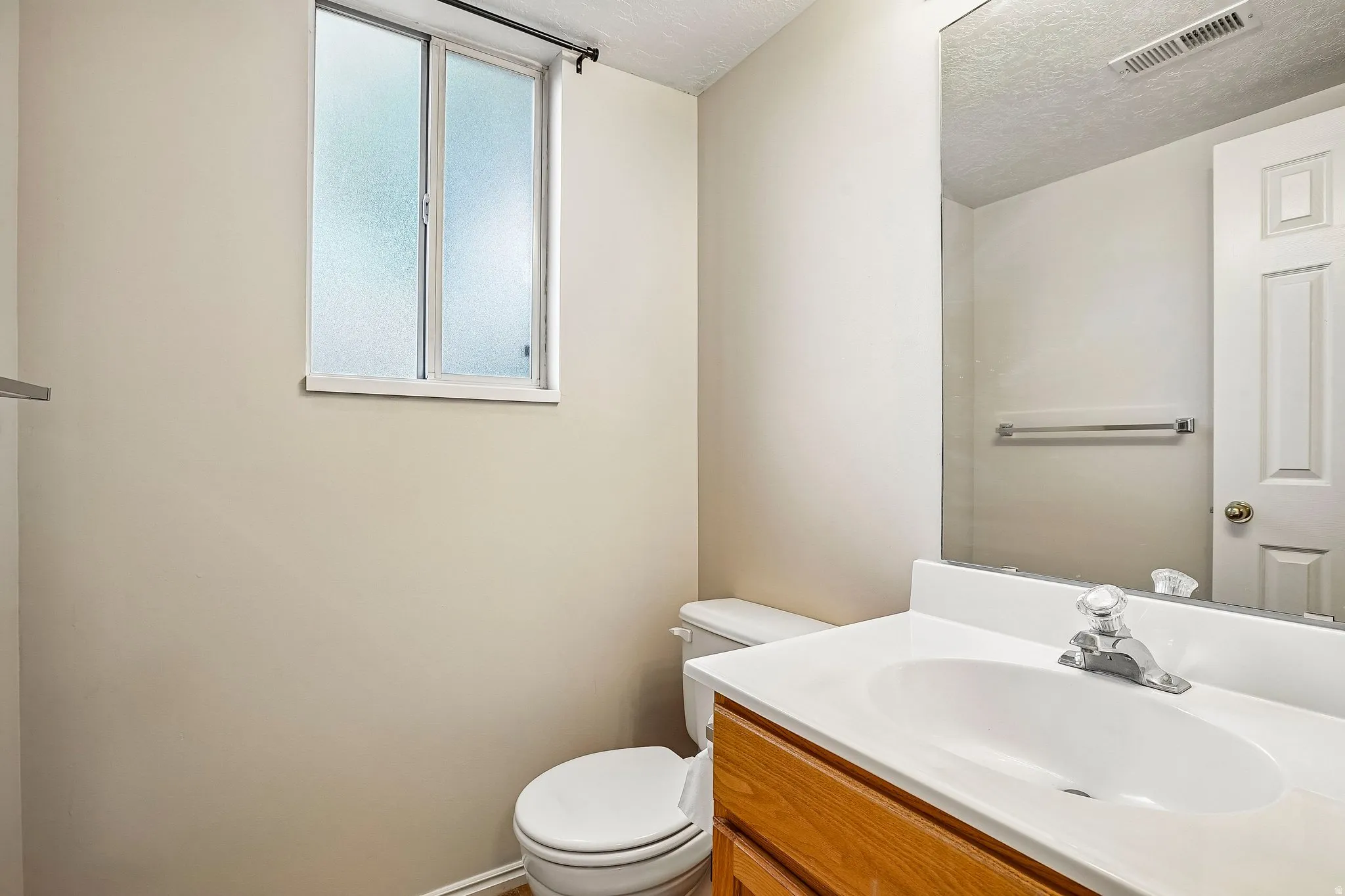 Bathroom featuring a wood-finish vanity with an integrated sink and chrome faucet, a large wall-mounted mirror, and neutral wall paint