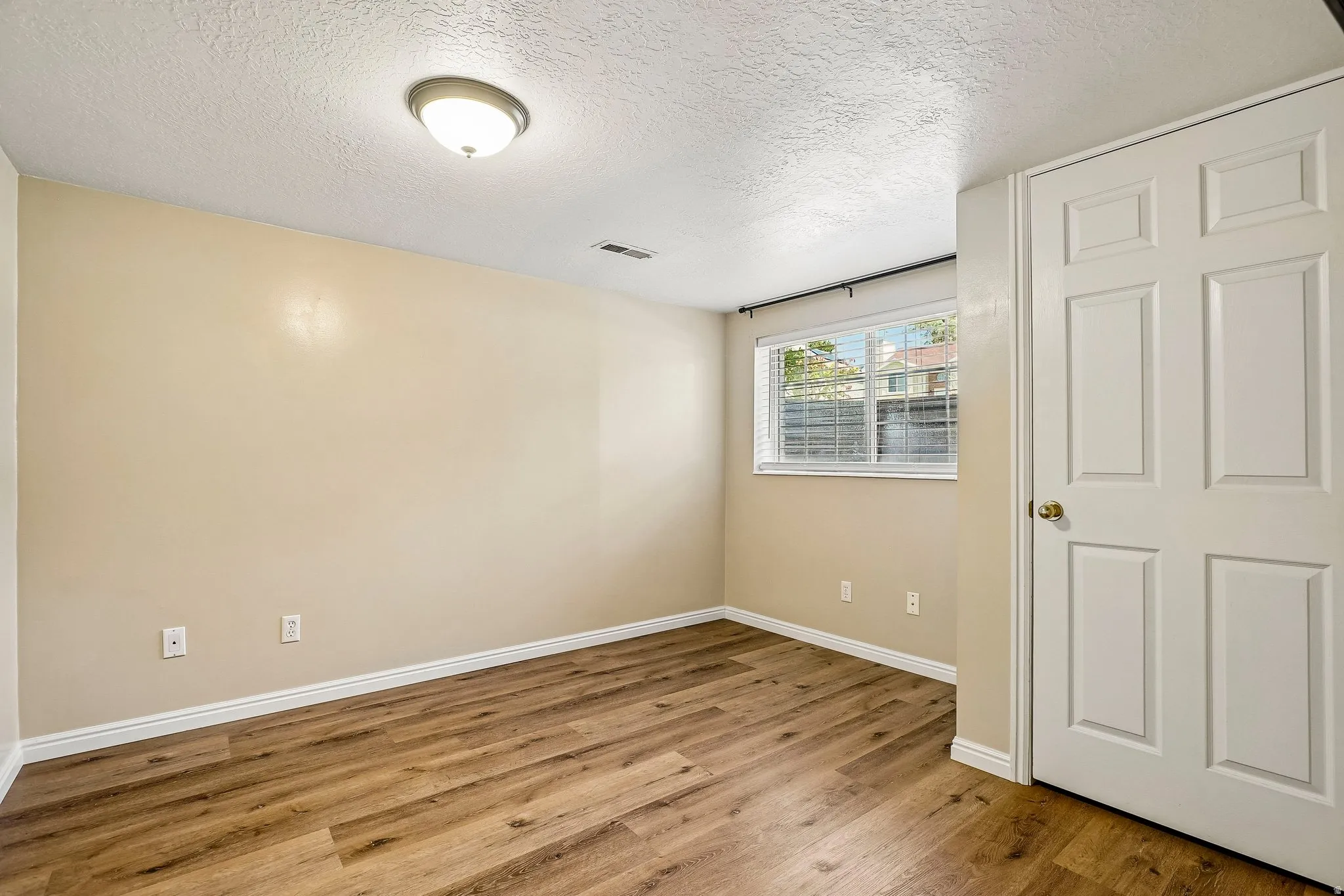 Spacious room featuring wood-finish flooring, neutral-toned walls, and white baseboards