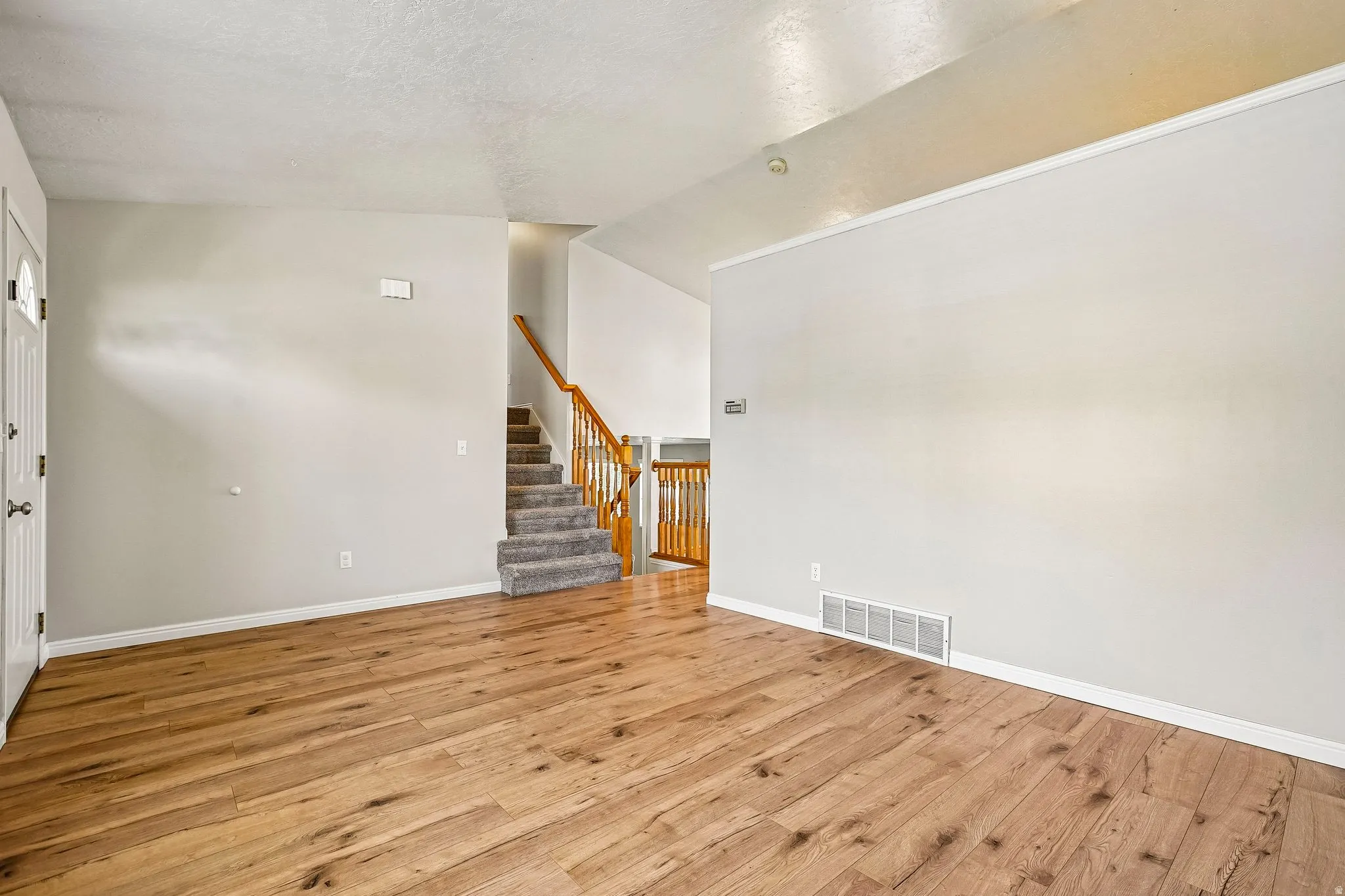Spacious room featuring wood-finish flooring, light gray wall tones, and white baseboards
