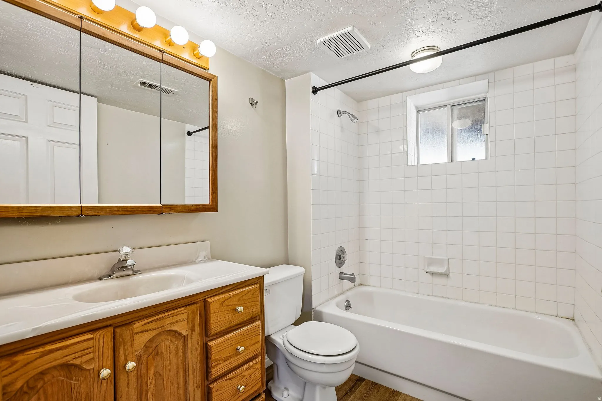 Bathroom featuring a wood-finish vanity with an integrated sink, tri-fold medicine cabinet, and a five-light fixture
