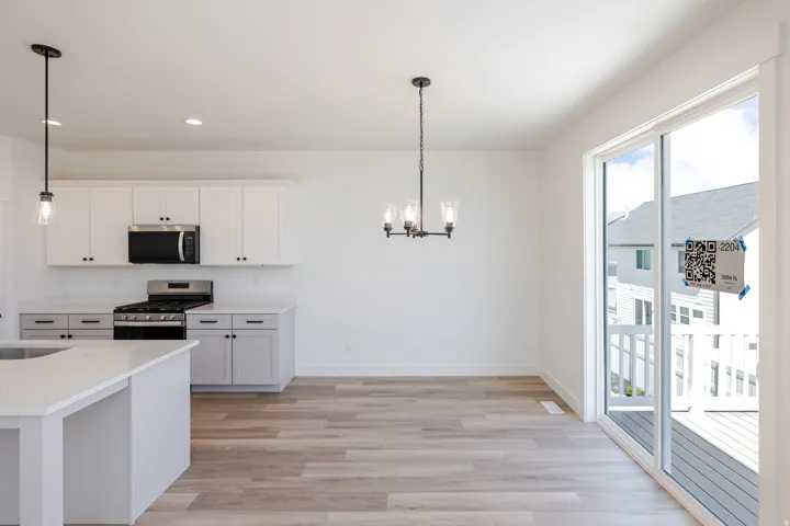 Kitchen and dining area featuring white cabinetry, stainless steel appliances, wood-finish flooring, and a sliding glass door to an outdoor deck