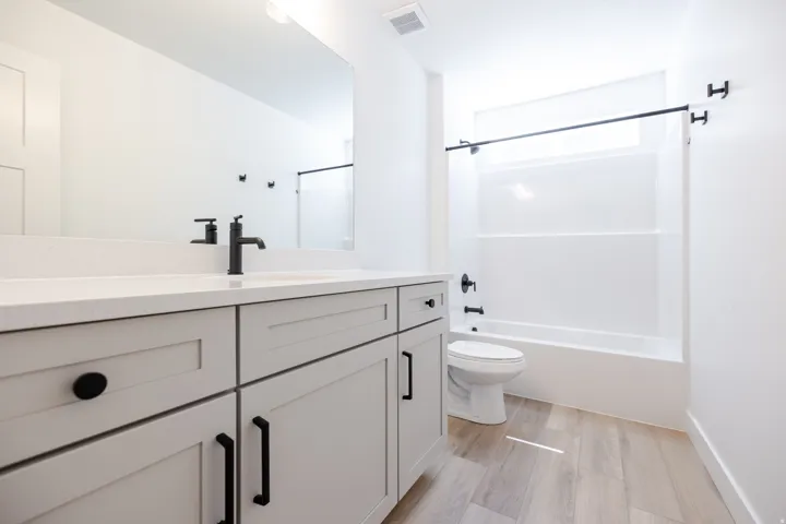 Light-toned wood-finish flooring complements the light gray vanity with black hardware