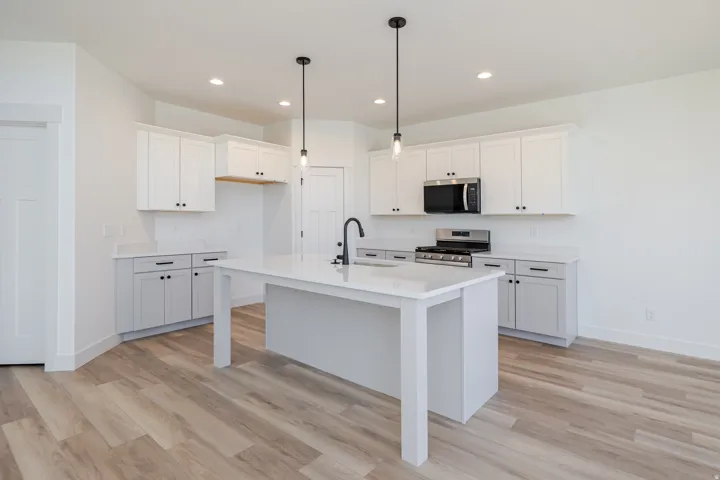 Kitchen featuring white cabinetry, light-toned countertops, a central island, stainless steel appliances, and wood-finish flooring