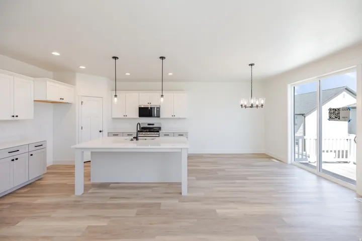 Open-concept living area featuring wood-finish flooring, a kitchen island with seating, white cabinetry, recessed lighting, and sliding glass doors leading to an exterior deck