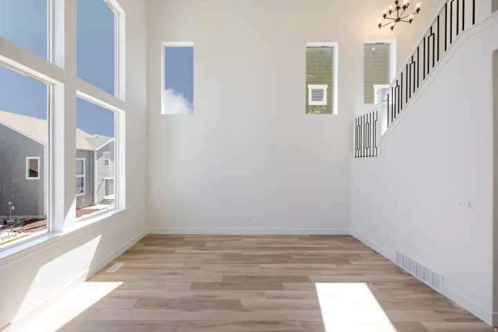 Vaulted ceiling with a contemporary chandelier, large picture windows, wood-finish flooring, and a staircase with decorative metal balusters