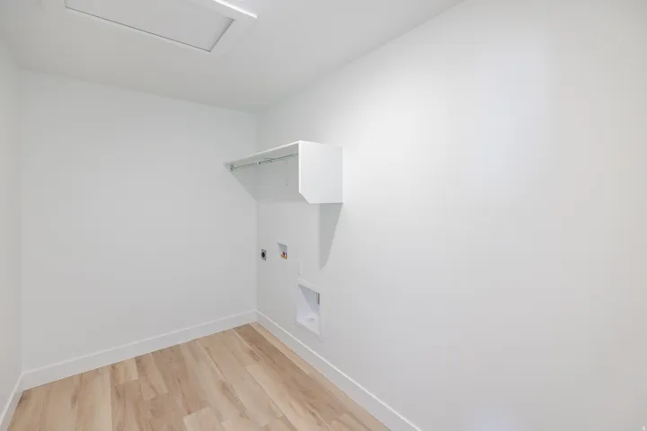 Wood-finish flooring with white baseboards, wall-mounted shelving, and utility hookups