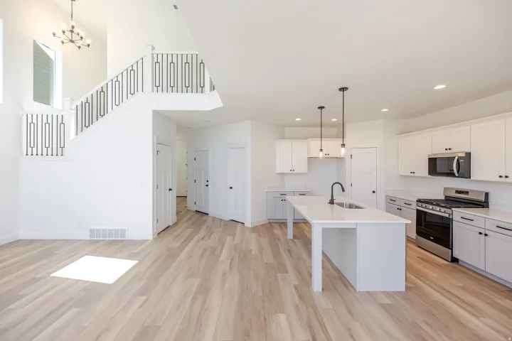 Open-concept living space with wood-finish flooring, a contemporary kitchen island with seating, stainless steel appliances, white cabinetry, and an open staircase with modern metal railings