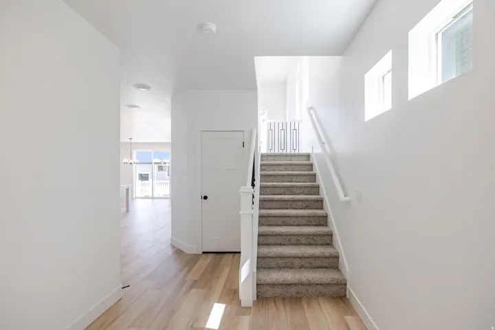 Entryway featuring wood-finish flooring, white walls, a carpeted staircase with white railings, and upper wall windows
