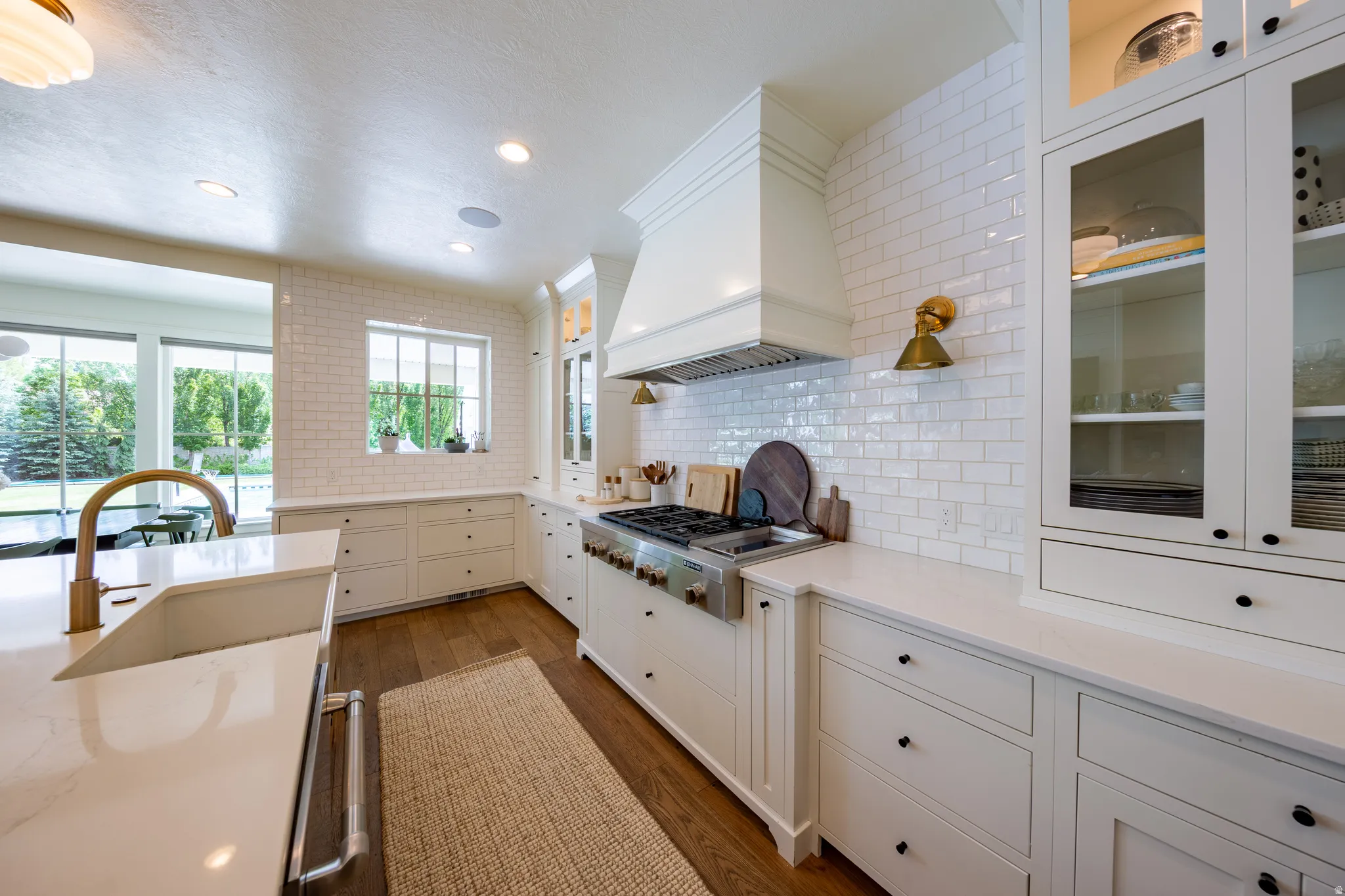 Gourmet kitchen featuring a professional-grade range, custom range hood, subway tile backsplash, white shaker cabinetry with glass-front uppers, and stone countertops