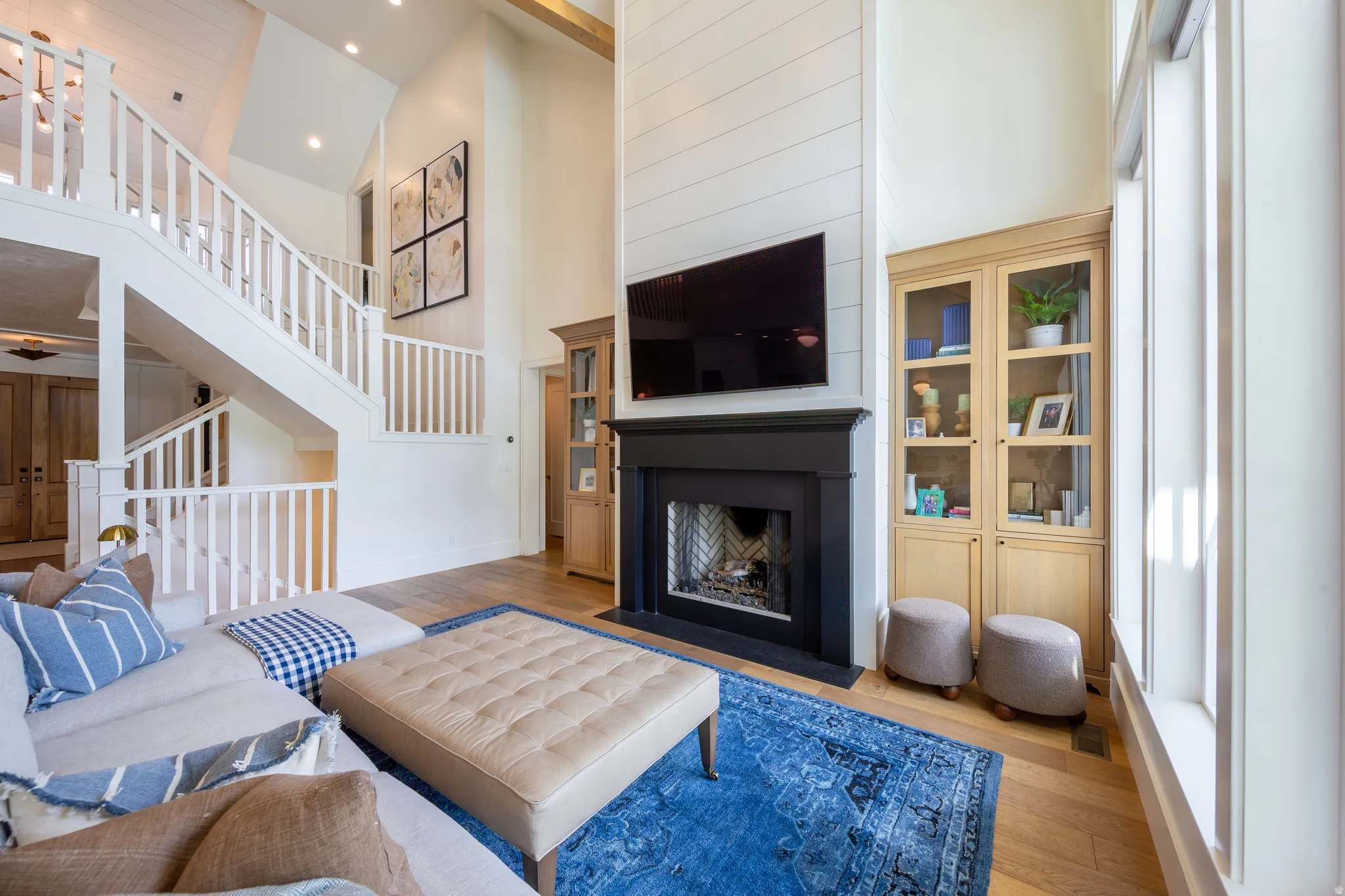 Spacious living area featuring a two-story shiplap fireplace surround with a black mantel, recessed lighting, and built-in cabinetry with glass doors