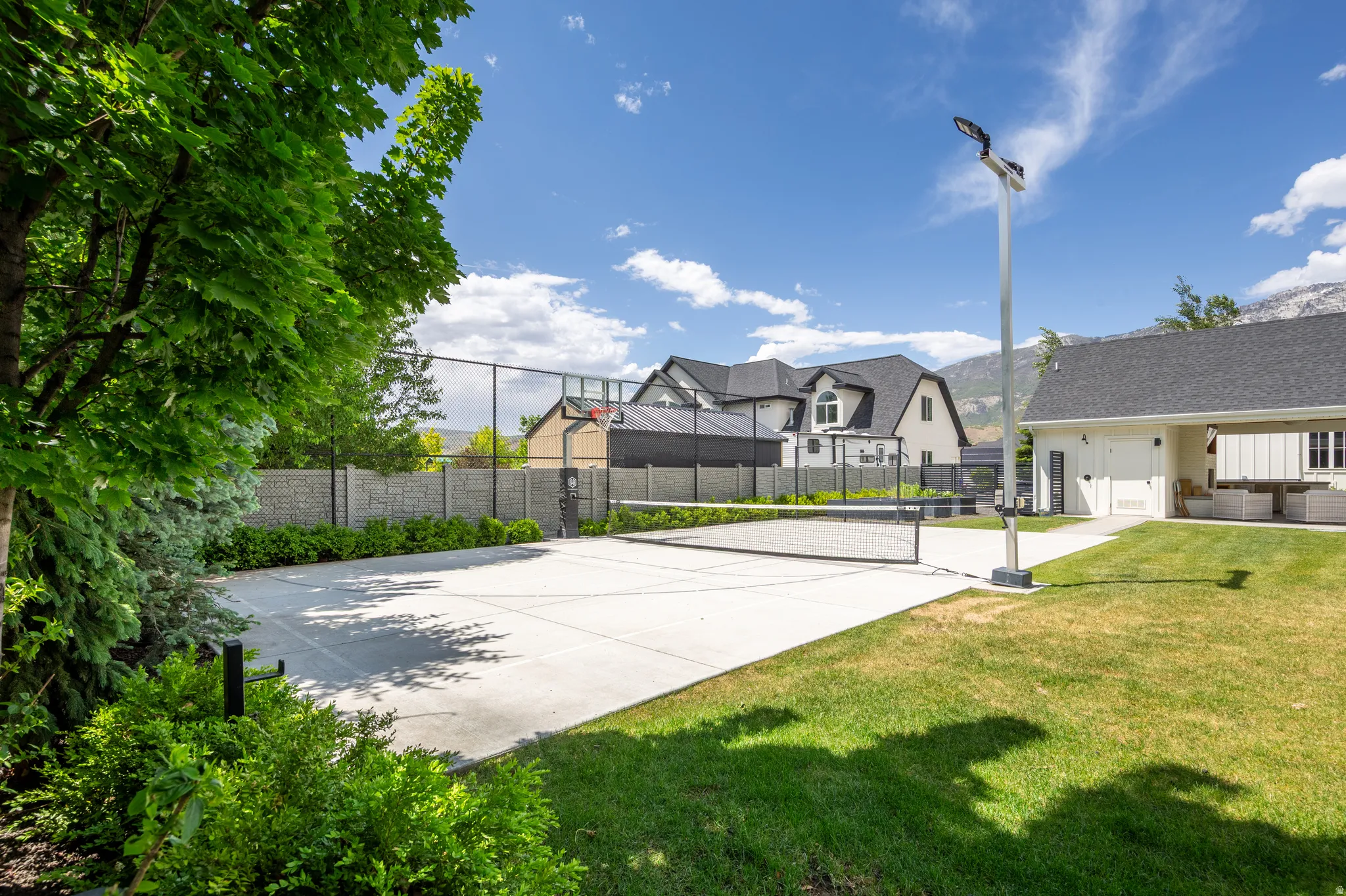 Hardscaped sport court with a net, basketball hoop, and perimeter fencing