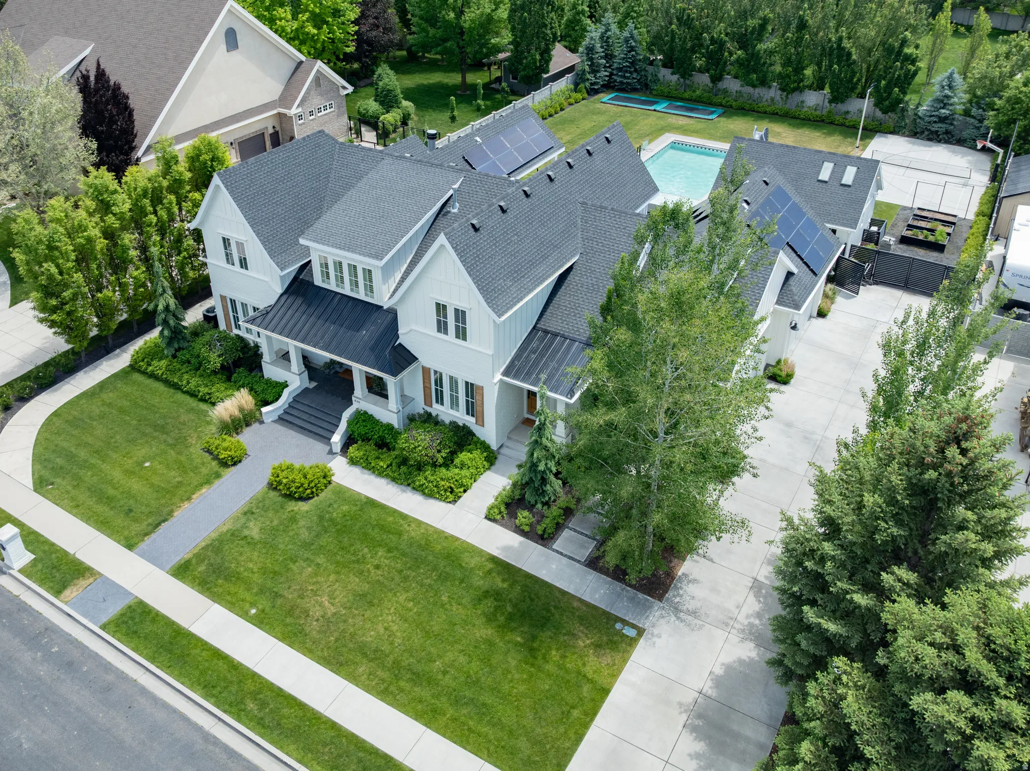 White siding residence featuring multiple gables and dormer windows, a covered front porch, an in-ground swimming pool, a concrete driveway, and solar panels