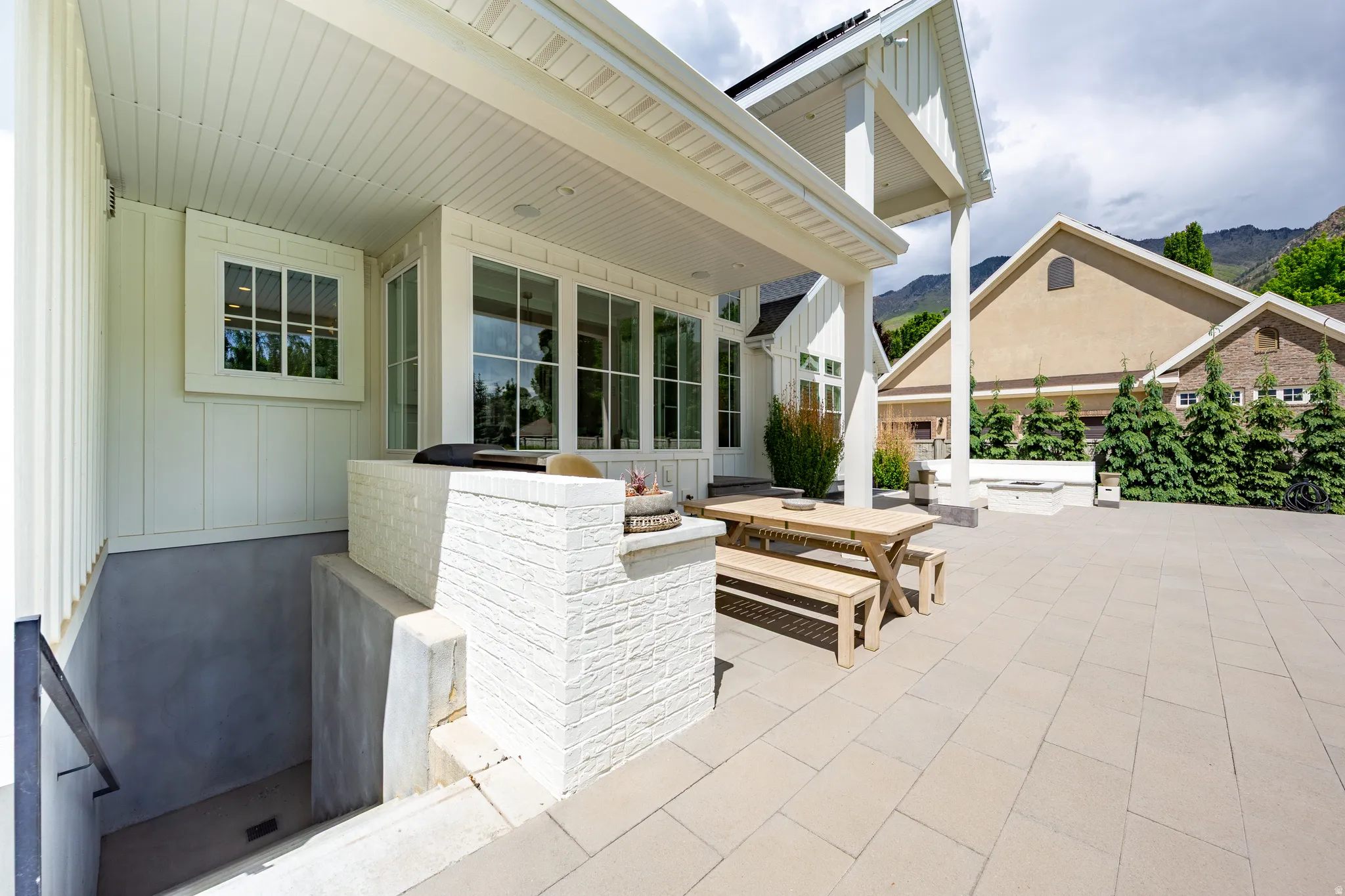 Spacious outdoor patio featuring light-toned paver flooring, a covered porch with white columns, and large windows