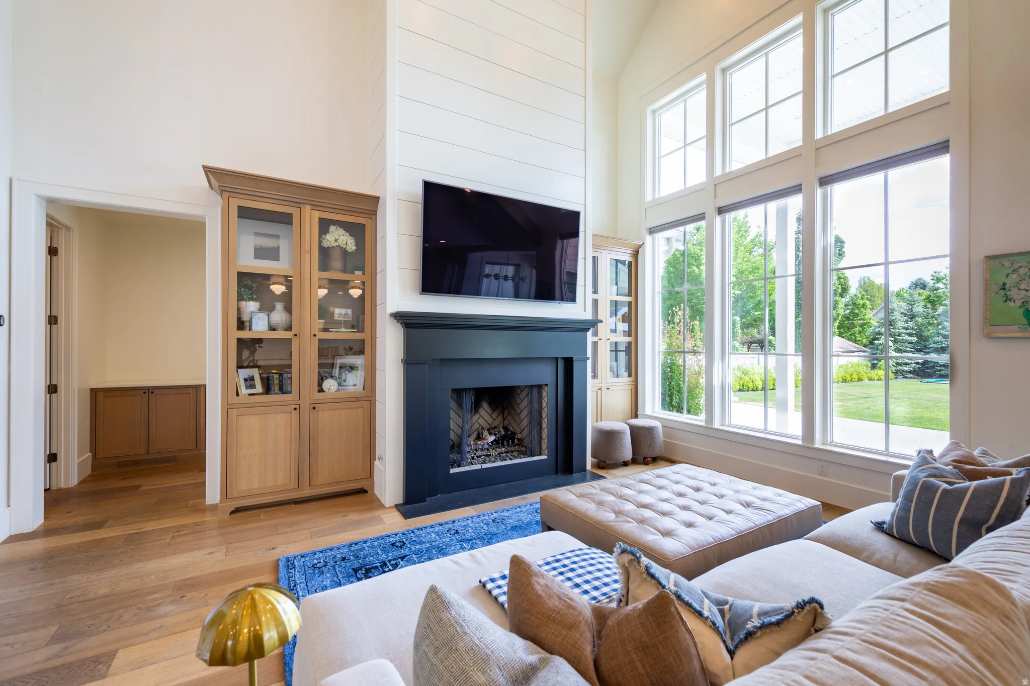 Spacious living area featuring double-height ceilings with shiplap accents, wood-finish flooring, and a dark-toned fireplace with a built-in hearth