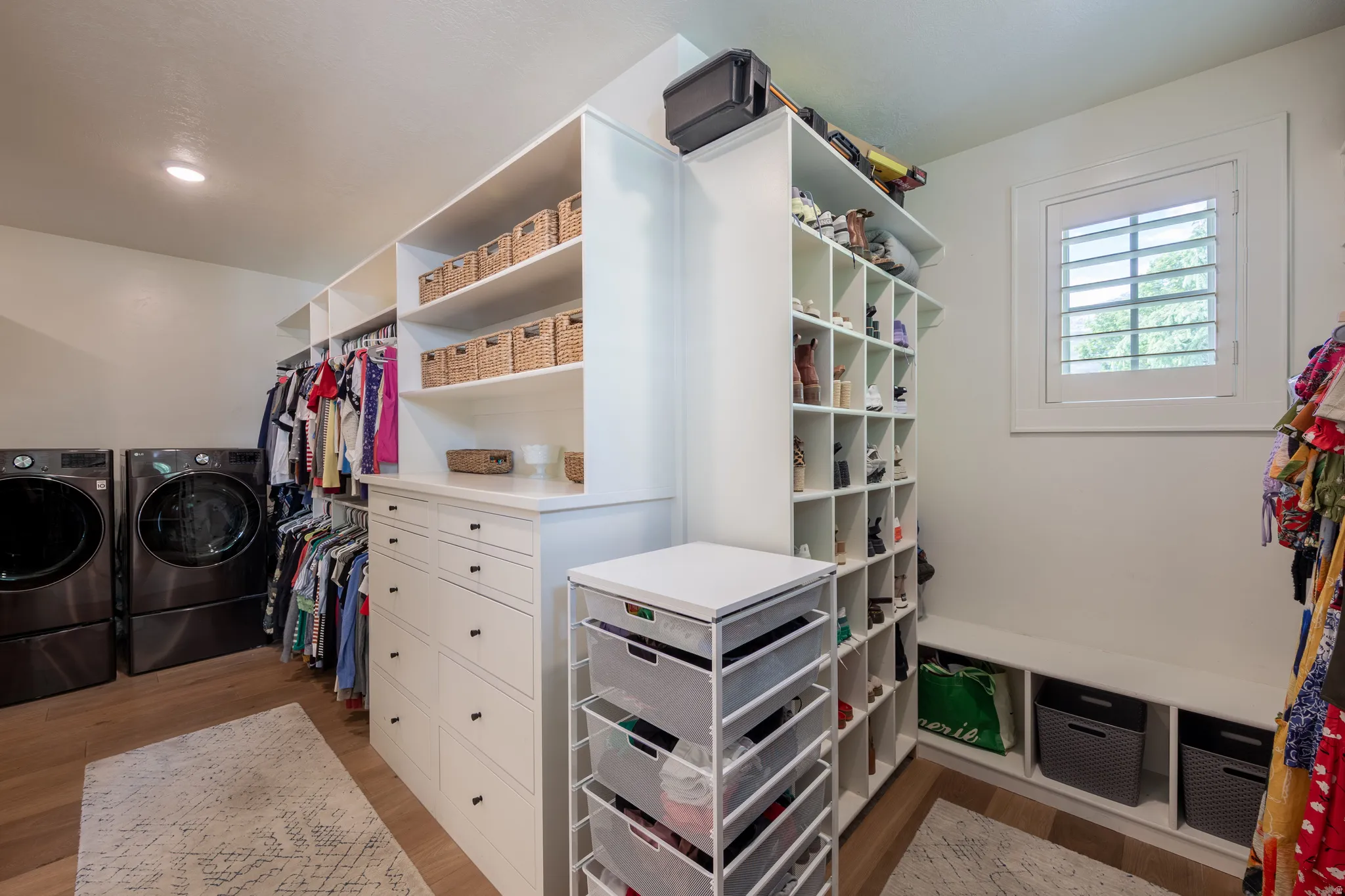Custom closet organization system featuring white cabinetry, built-in drawers with black hardware, and open shelving