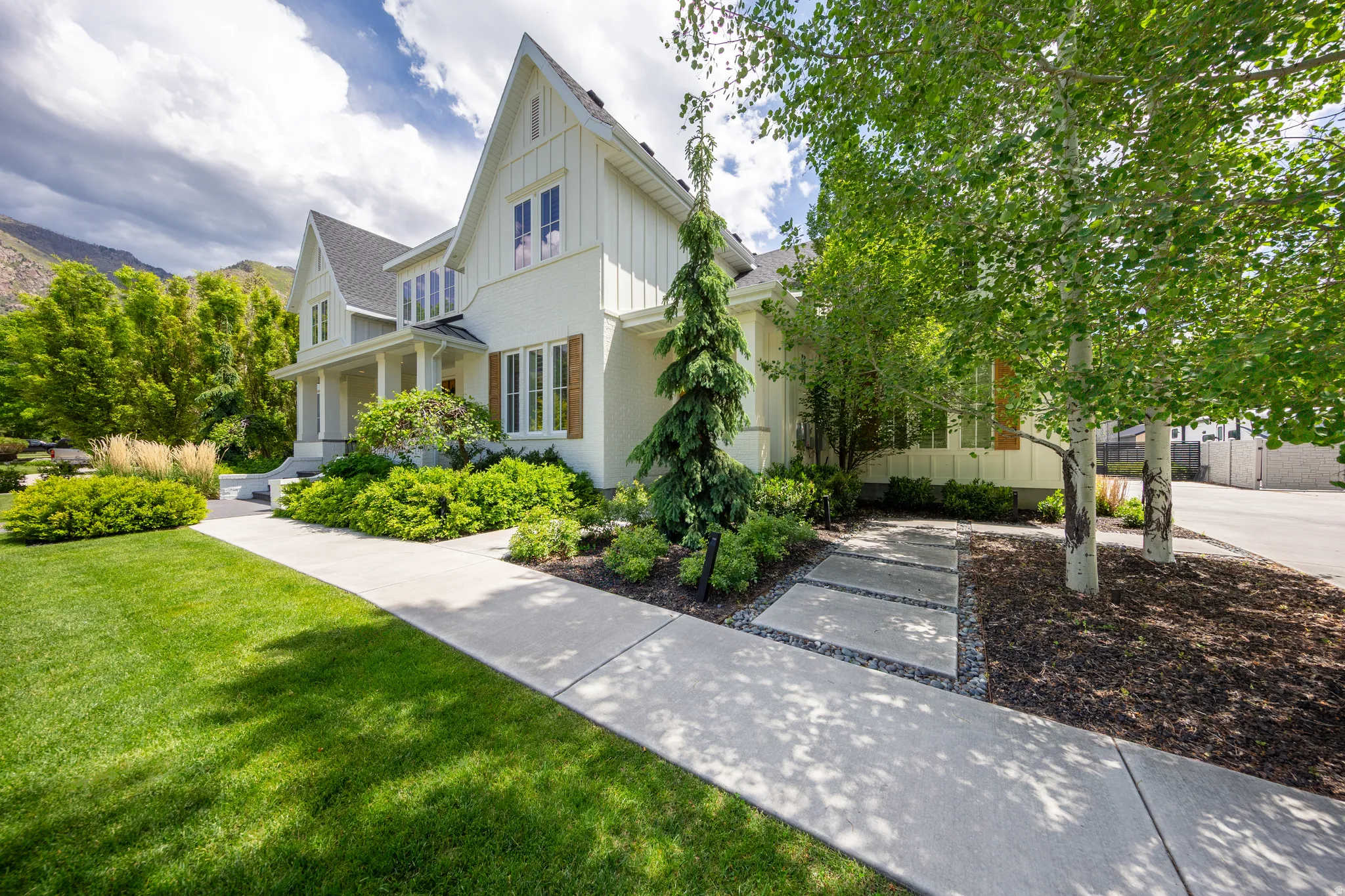 White-sided residence featuring a covered porch with columns, a prominent gabled roofline, and wood shutters