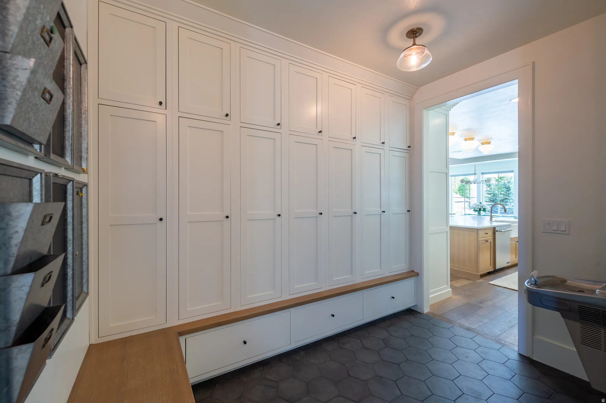 Built-in white shaker-style cabinetry with black hardware, integrated bench seating, hexagonal dark tile flooring, recessed ceiling lighting, and a wide entryway
