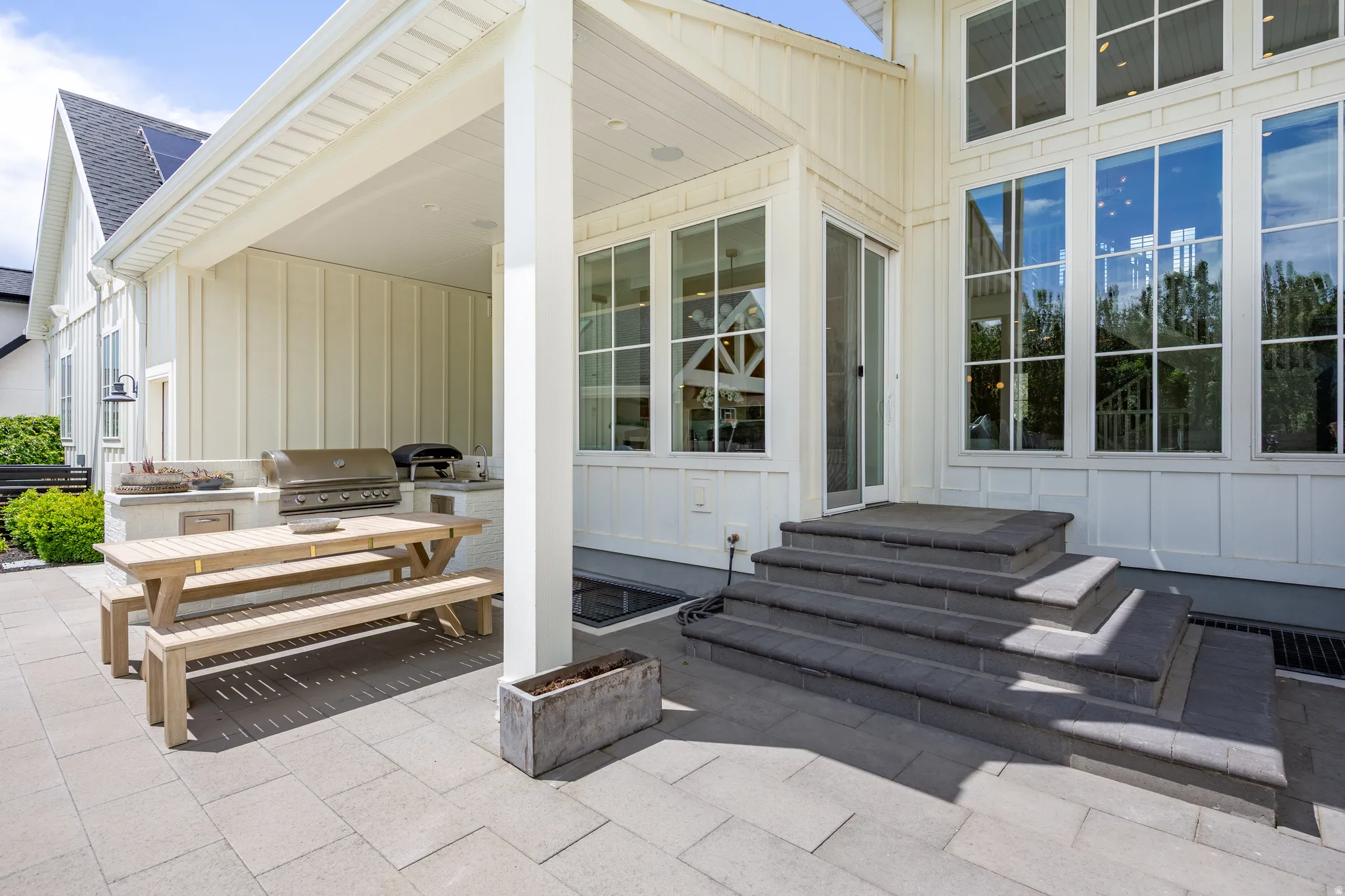 Expansive paver patio featuring a covered outdoor kitchen with a built-in grill, a separate outdoor oven, and a wood picnic table