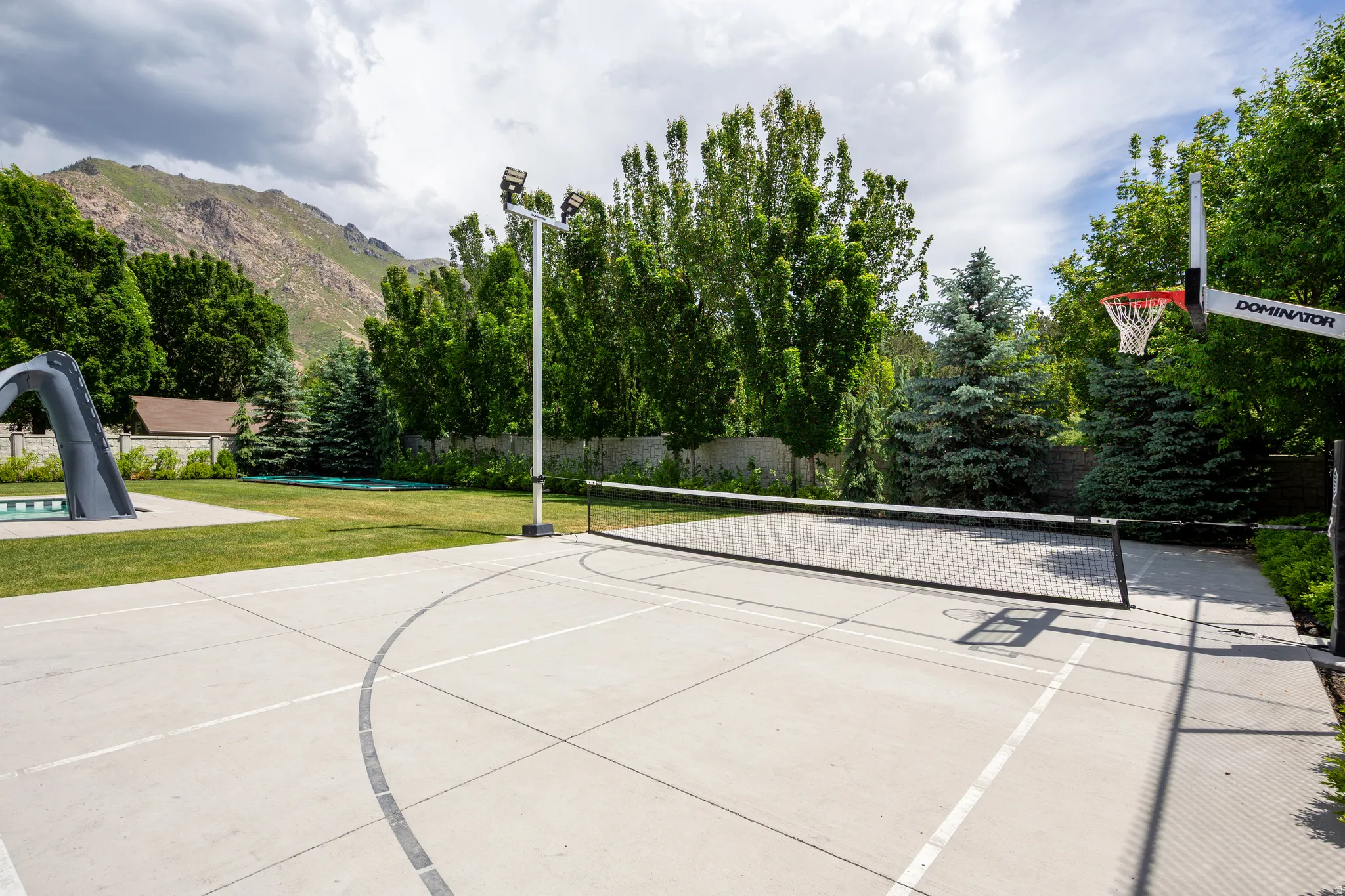 Outdoor concrete sports court featuring a basketball hoop, net for court sports, and integrated lighting