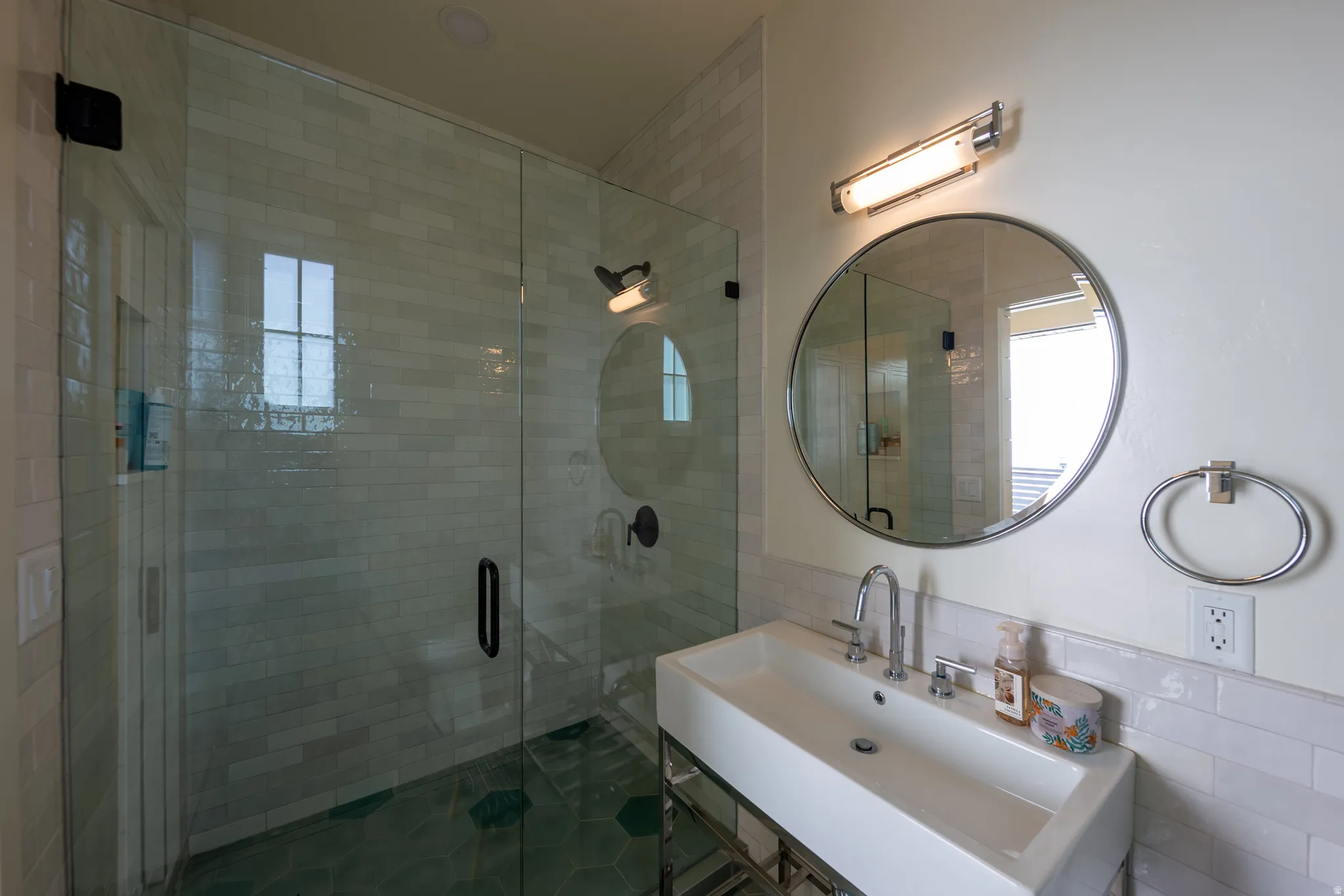 Modern bathroom featuring a rectangular vessel sink with polished chrome fixtures, a frameless glass shower enclosure, and a round wall-mounted mirror