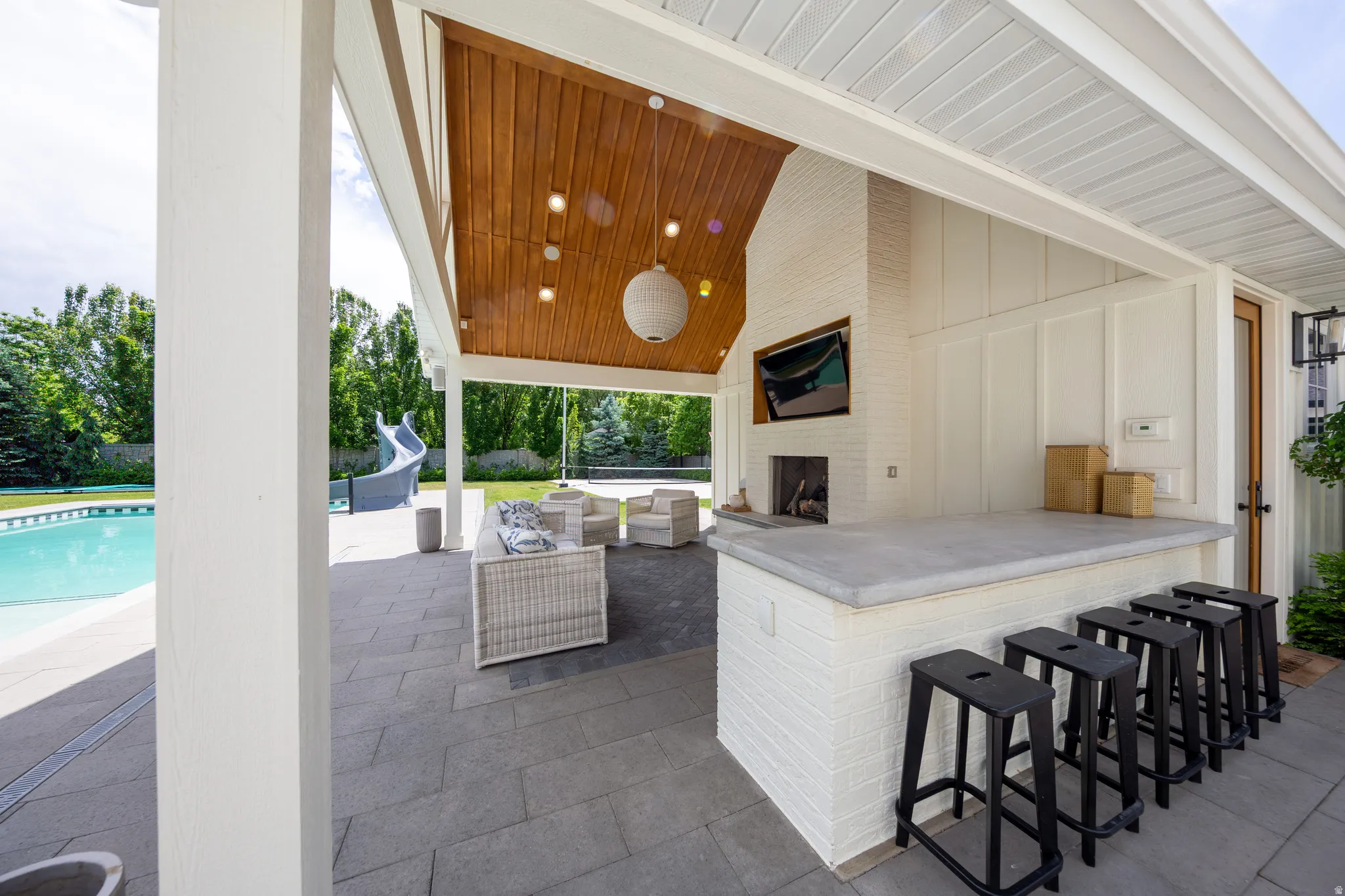 Covered outdoor patio featuring a wood-finish ceiling, built-in fireplace, white brick wet bar with seating, and a large swimming pool