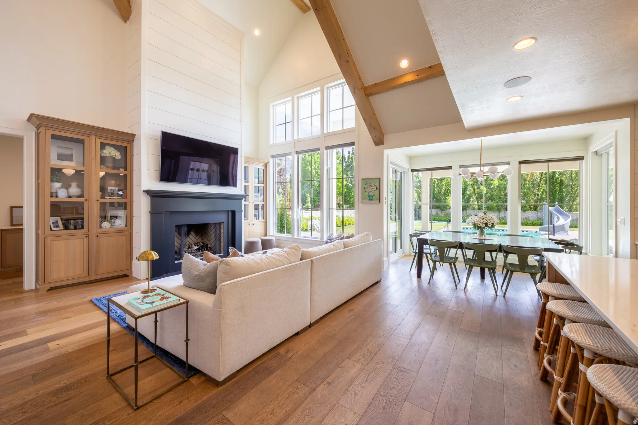 Spacious living area featuring wood-finish flooring, a vaulted ceiling with exposed wood beams, and a dark mantel over a fireplace