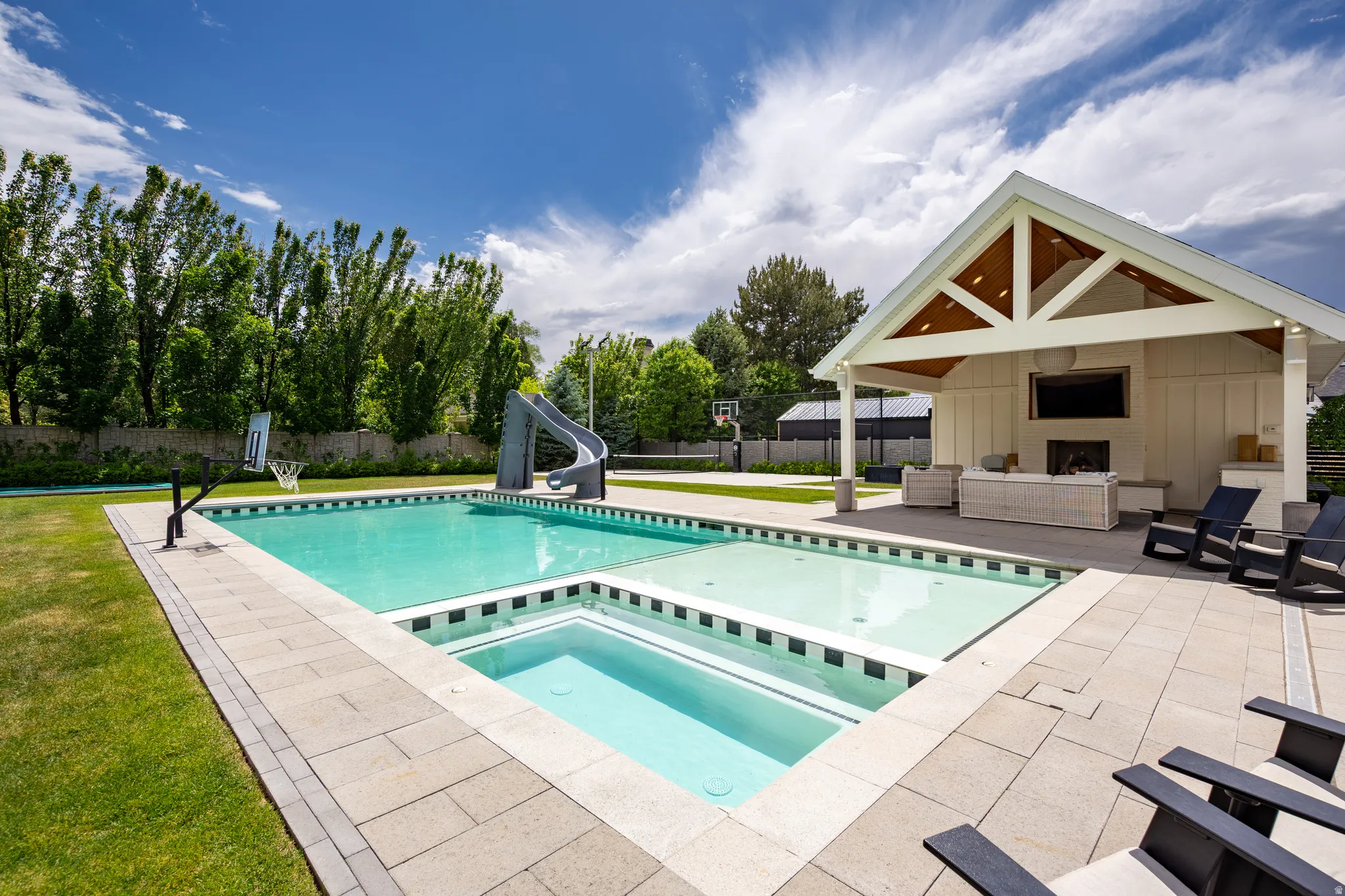 Expansive outdoor area featuring a swimming pool, integrated spa, and a pool house with a vaulted ceiling and exposed beams