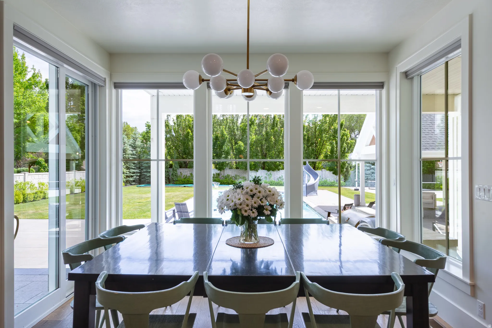 Bright dining space featuring a contemporary chandelier with globe lights, expansive windows, multiple glass sliding doors, and wood-finish flooring