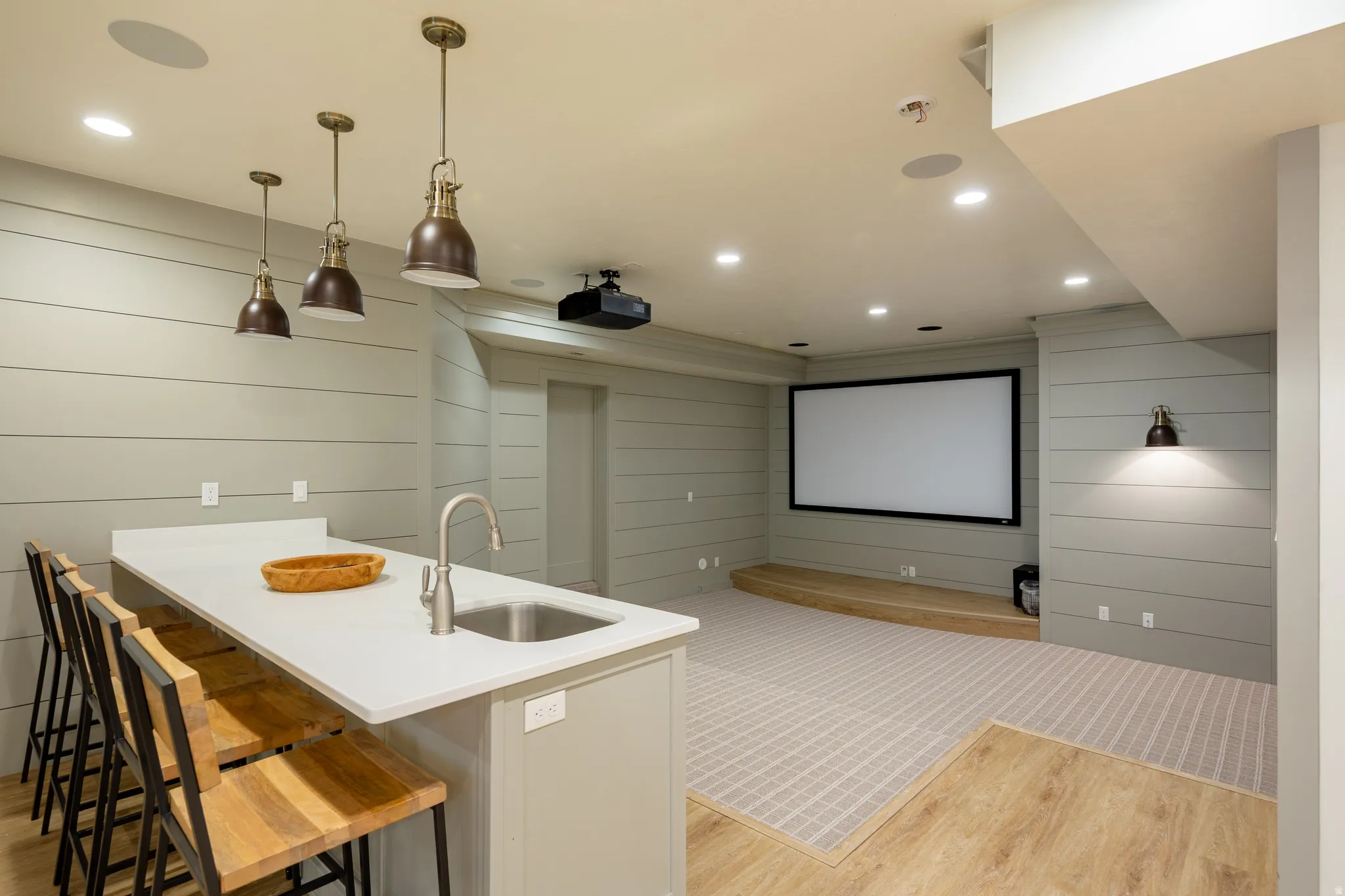 Entertainment space featuring a white quartz-finish island with integrated sink, three industrial-style pendant lights, shiplap wall accents, a projector screen, and recessed lighting