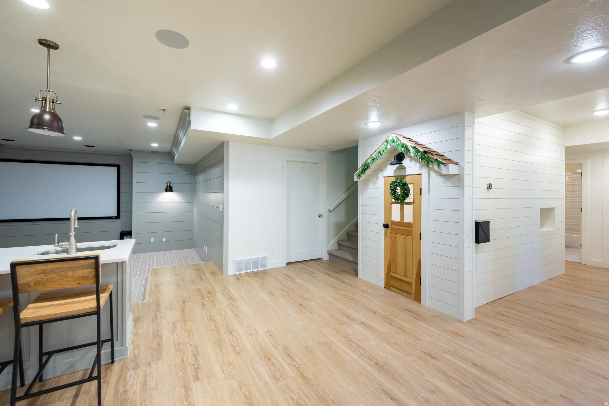 Open-concept recreational space featuring wood-finish flooring, recessed lighting, and an integrated wet bar with a white countertop and stainless steel sink