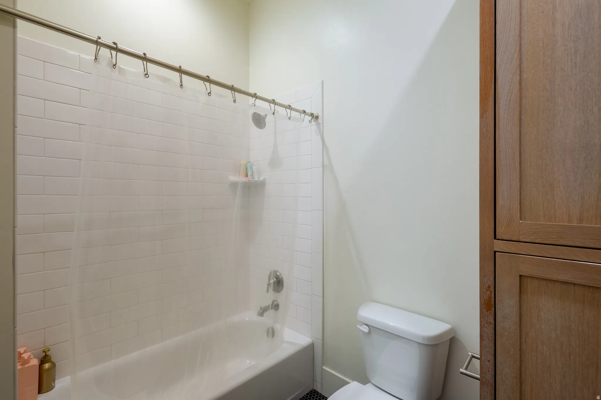 Bathroom featuring a white subway tile surround, a built-in tub, polished chrome fixtures, a white toilet, and wood-finish cabinetry