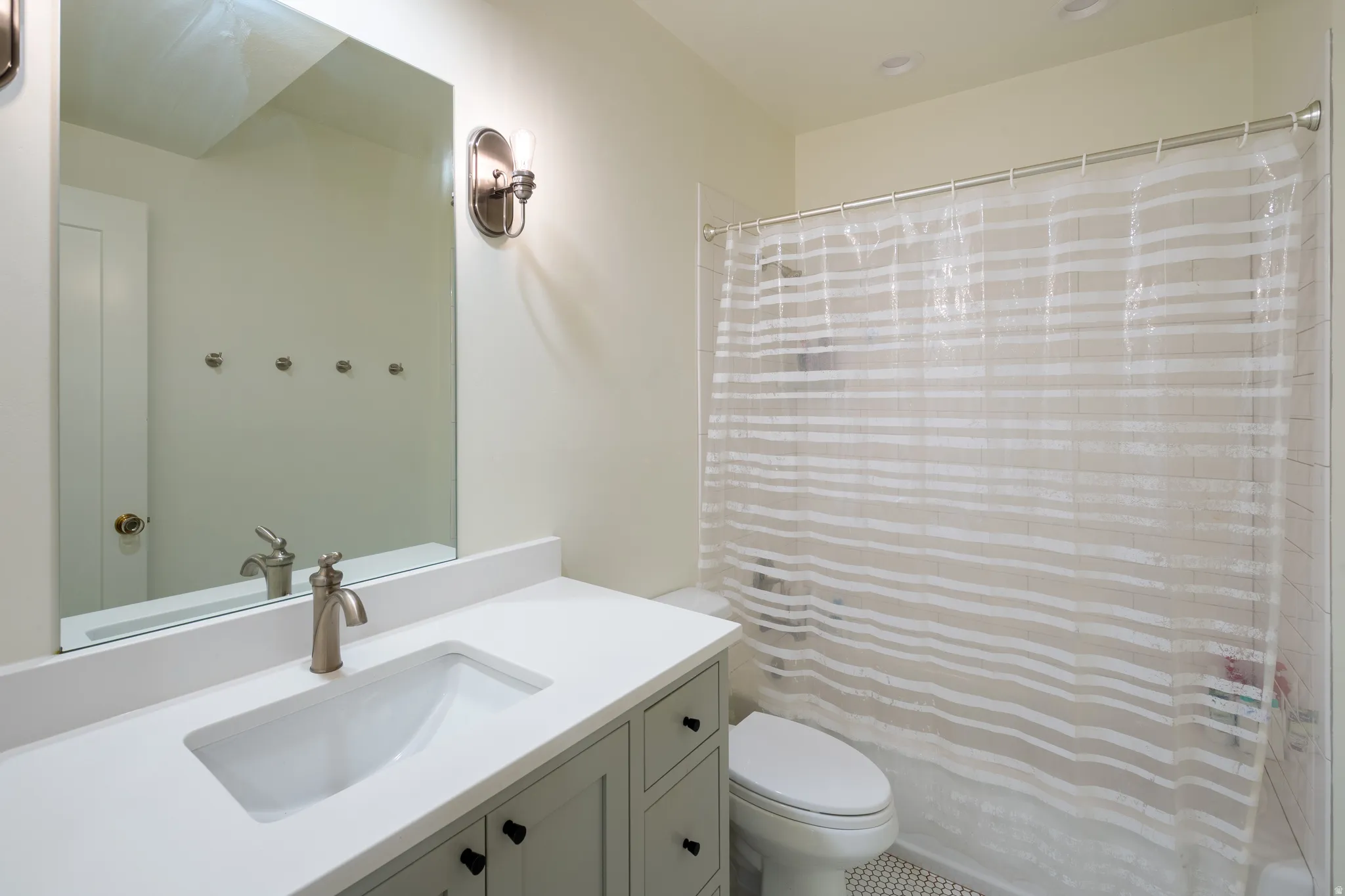 Bathroom featuring a light-toned vanity with shaker-style cabinetry, a white countertop with an integrated sink, a brushed nickel faucet, a large rectangular mirror, and a full shower with white subway tile surround and mosaic floor tile
