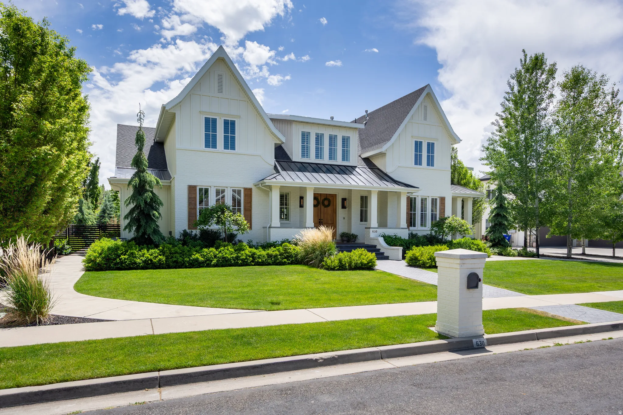 White exterior featuring board-and-batten siding, a dark pitched roof, and a covered front porch with columns