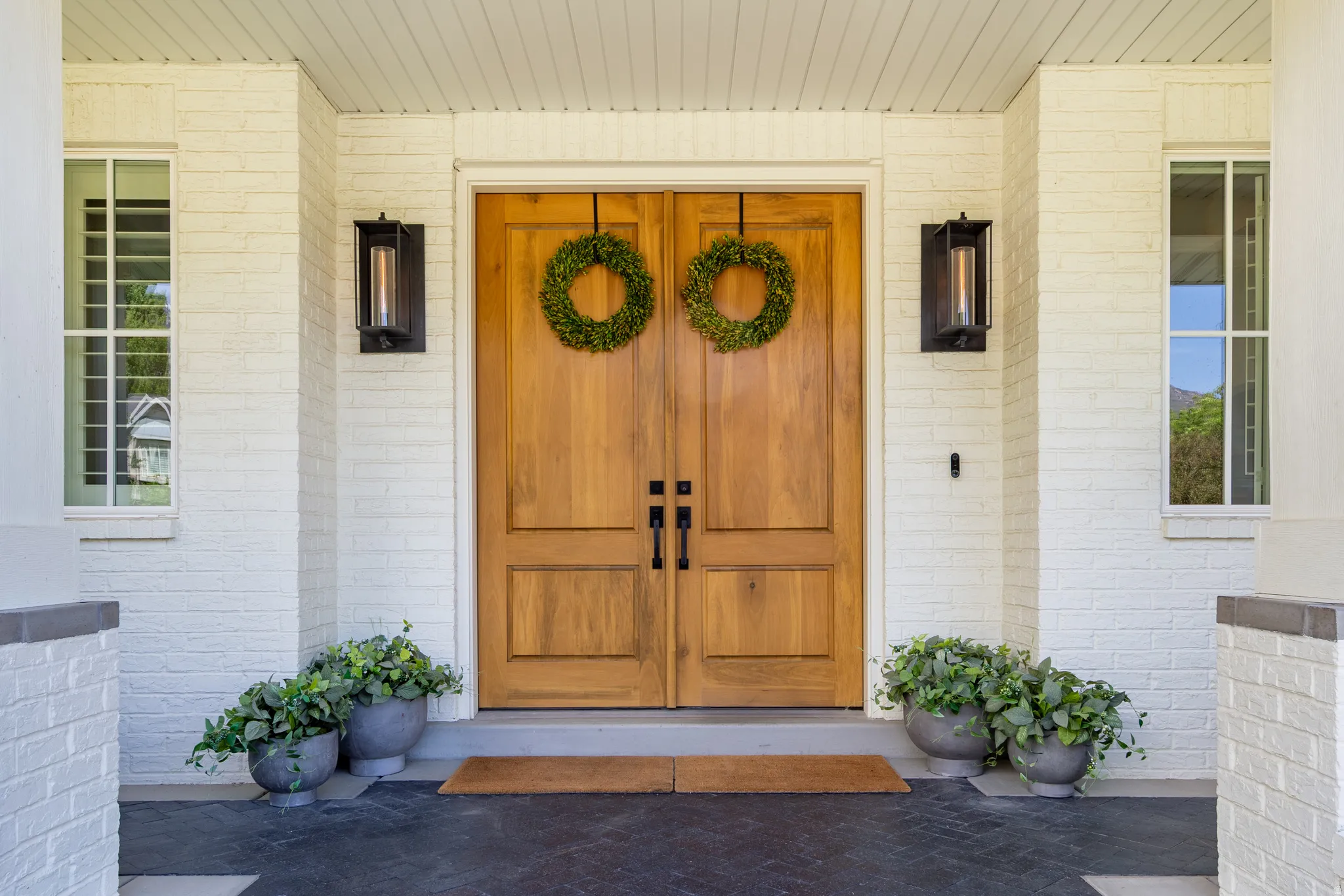 Double wood-panel entry doors featuring black hardware, flanked by modern wall-mounted light fixtures