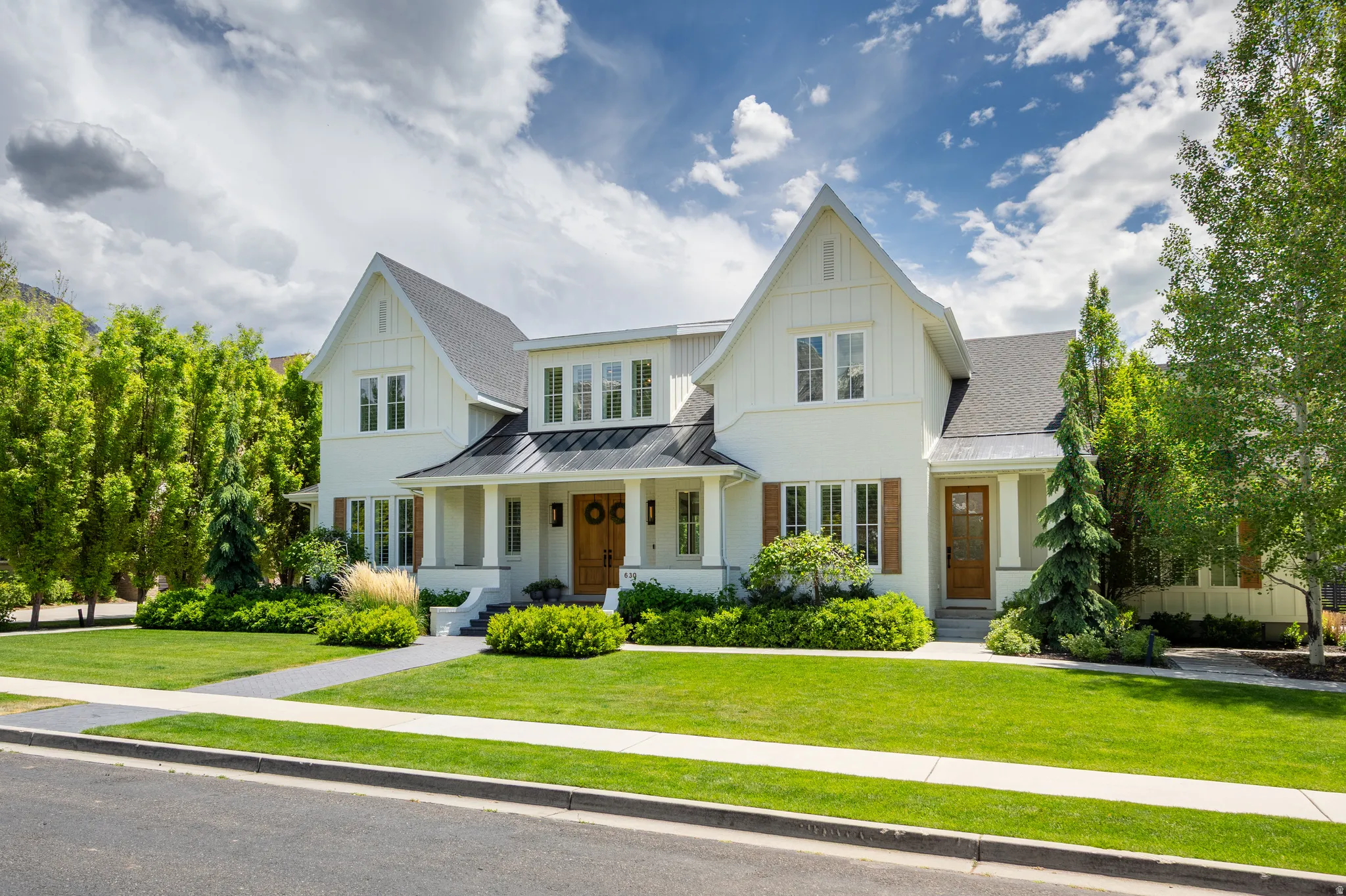 Gable-front home featuring white siding, brown wood shutters, a dark shingle roof, and a covered porch with white columns