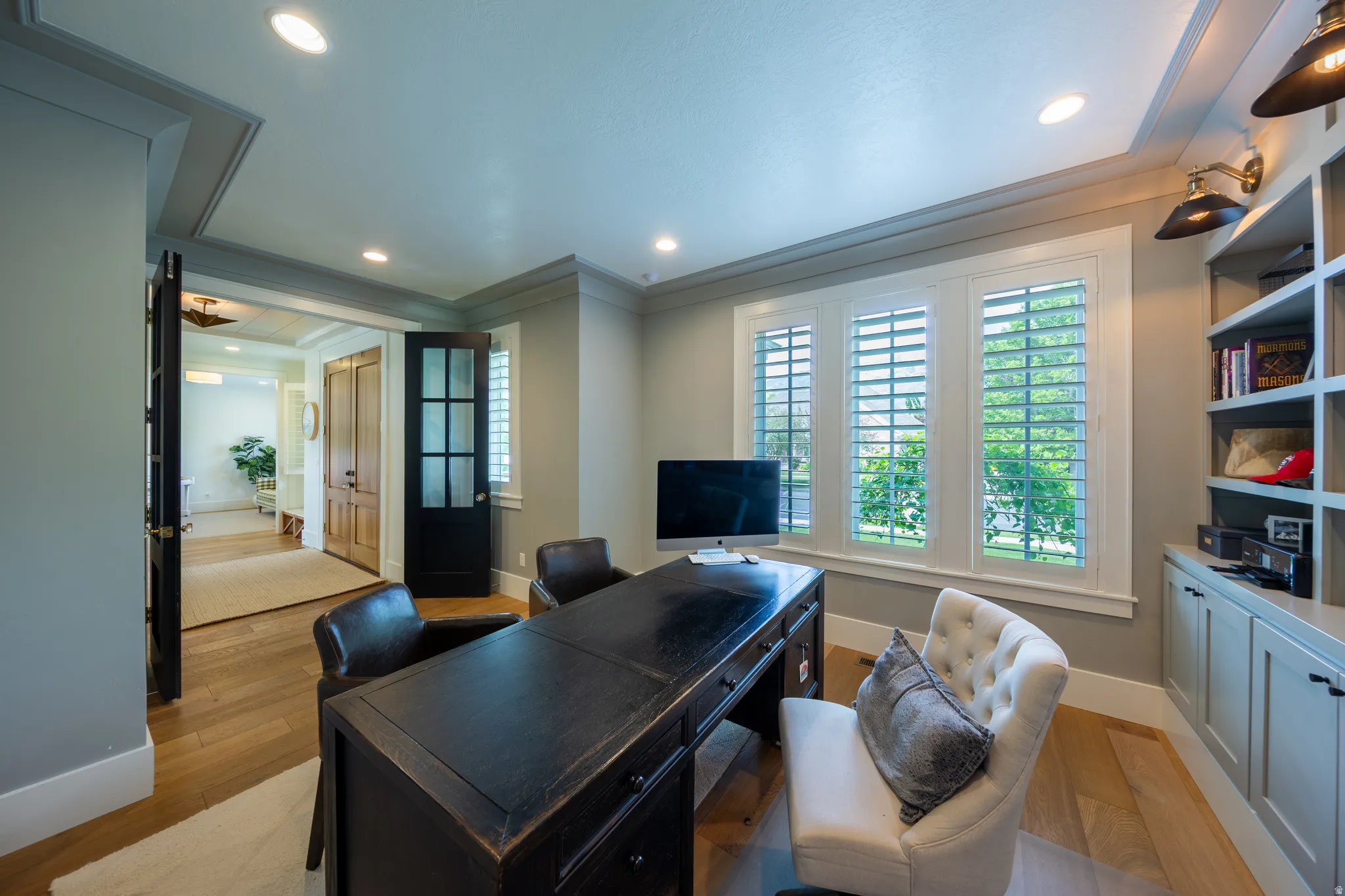 Office space featuring hardwood flooring, built-in shelving with cabinetry, a bay window with plantation shutters, recessed lighting, and crown molding