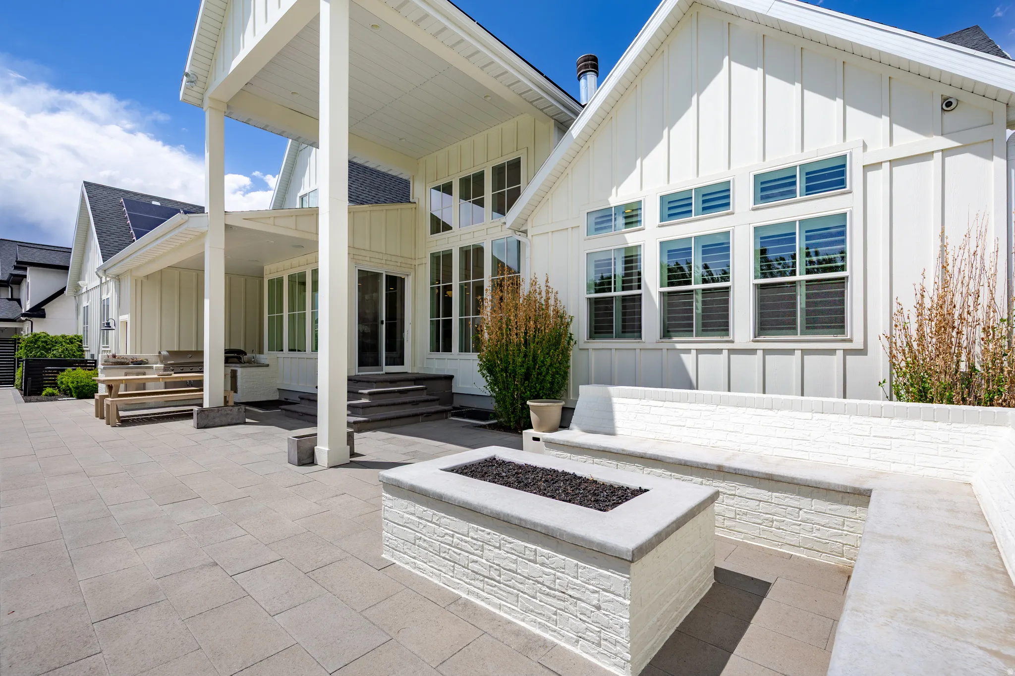 Expansive paver patio featuring a built-in fire pit with stone surround, integrated bench seating, and an overhead covered porch
