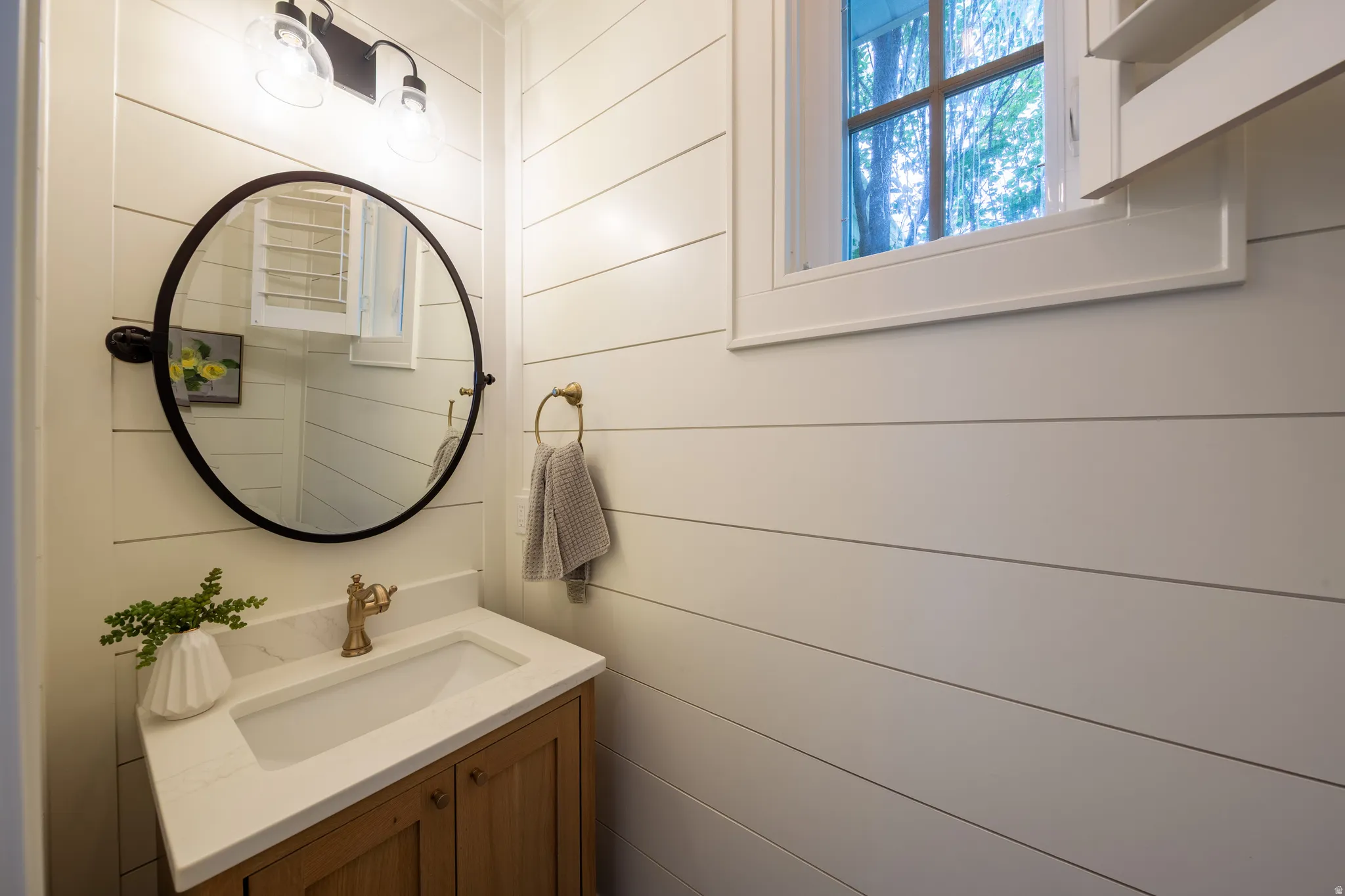Vanity area featuring a wood-finish cabinet with white countertop, integrated sink, and brass-tone faucet