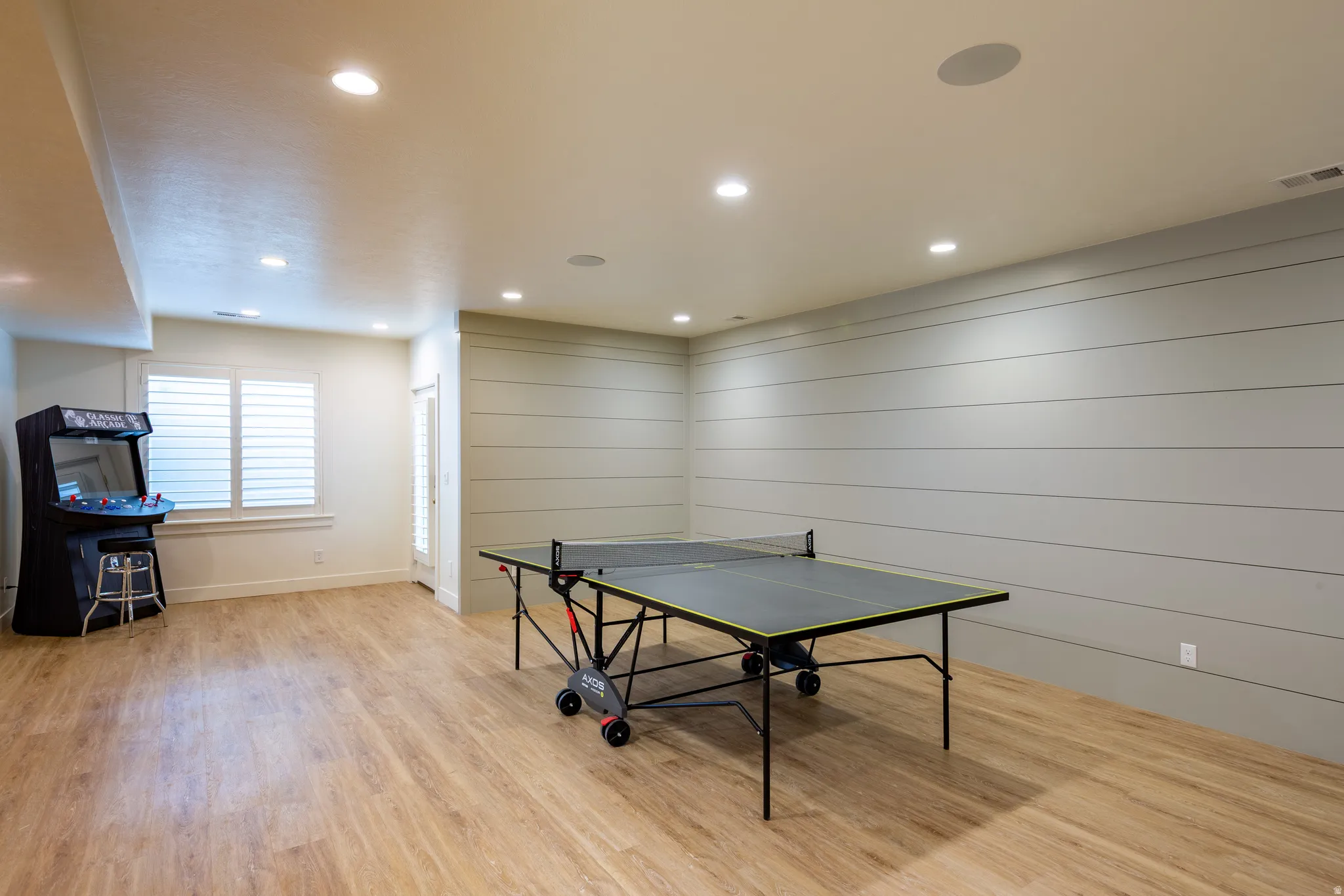 Spacious recreation room featuring wood-finish flooring, shiplap accent wall, recessed lighting, and built-in ceiling speakers